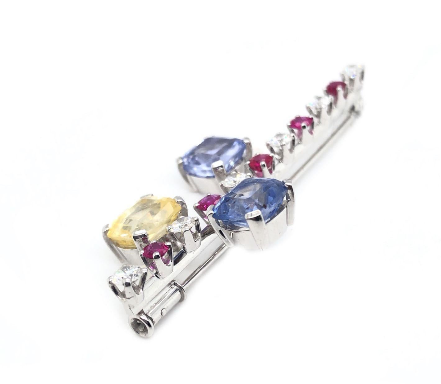 18kt white gold straight pin of alternating diamonds and rubies with 2 larger blue sapphires and 1 yellow sapphire.