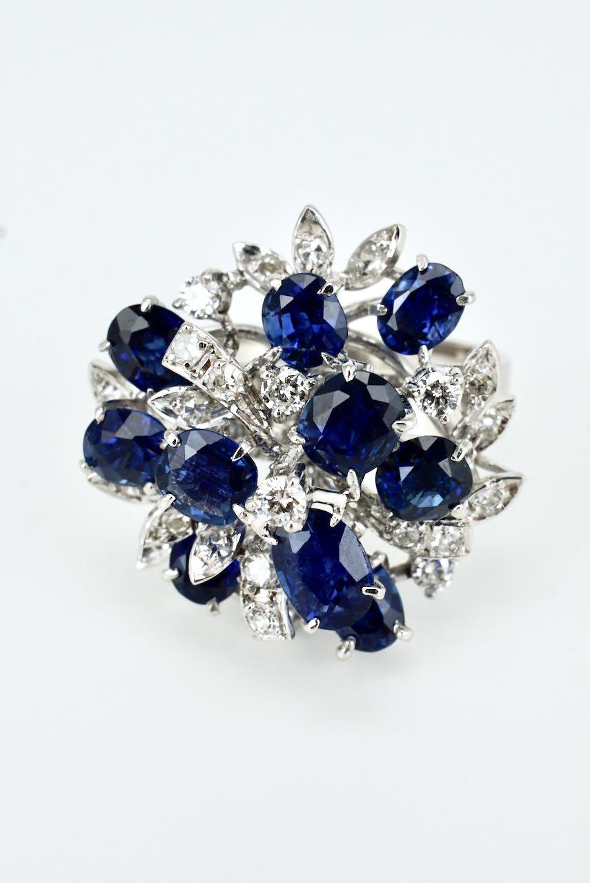 A cluster ring featuring 10 oval cut medium blue Ceylon sapphires set within a foliate design of 25 single cut diamonds on a flat tapered shank - a luscious combination of sapphires and diamonds in a freeform design which makes a real statement -