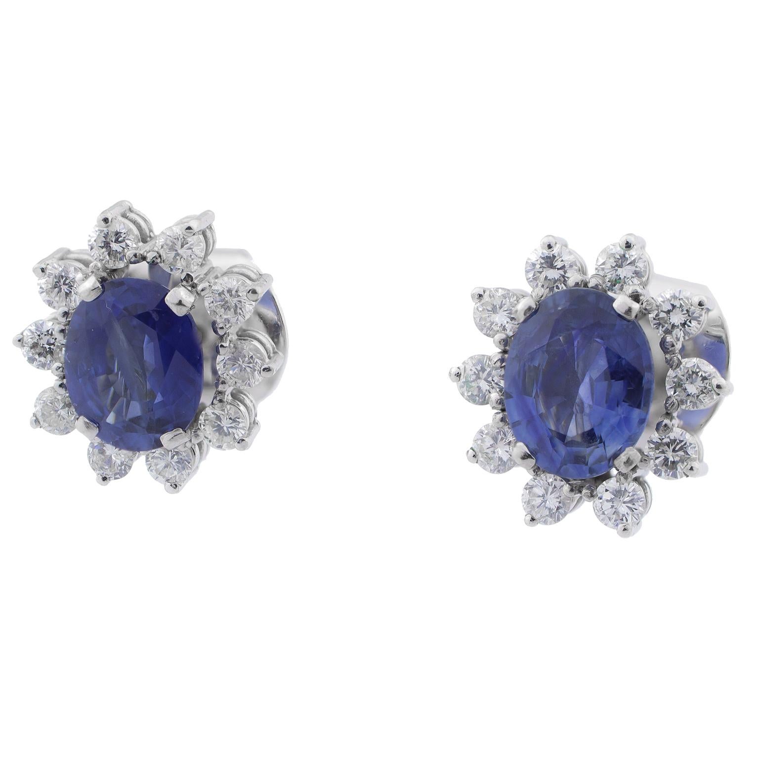 White gold earrings set with two oval cut blue sapphires with a total of 3.80 carats in weight, surrounded by 20 round brilliant cut diamonds totalling 1.00 carats.