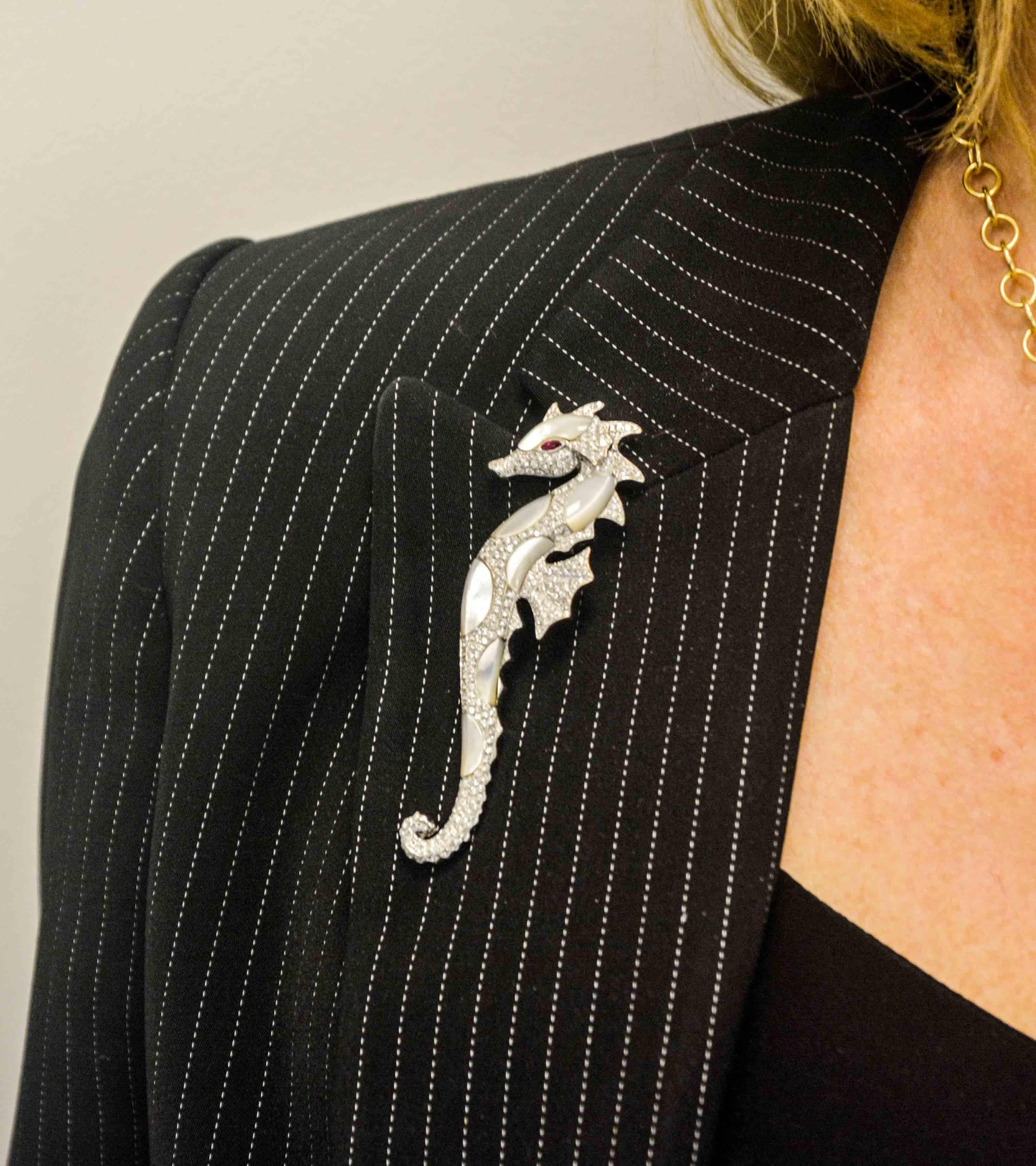 An exquisitely designed seahorse is crafted in 18 karat white gold. This dainty seahorse has ruby eyes (.02 ctw), abalone Mother-of-pearl and diamonds (2.50 carat total weight, G-H color, VS internal clarity). This brooch measures 3.5 inches and