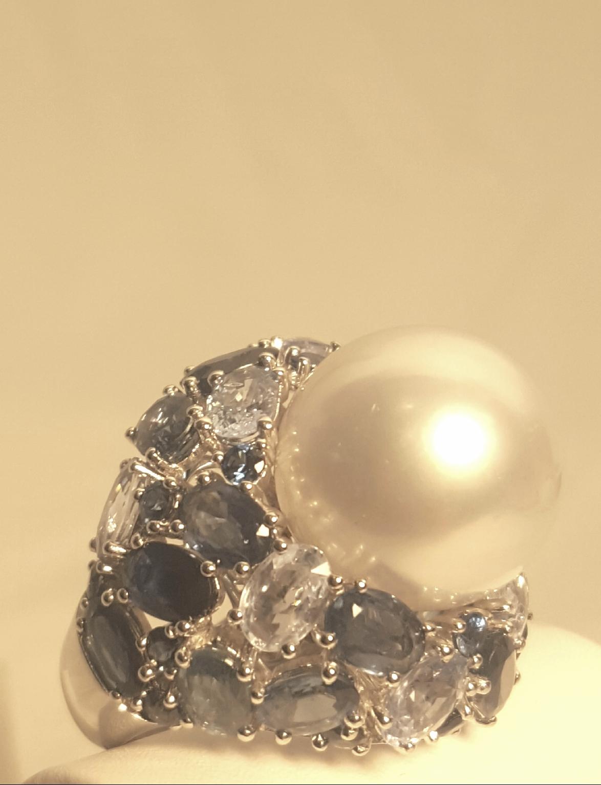 An exquisite ring!  Crafted in 18 karat white gold, this beauty boasts a 16mm white lustrous South Sea Pearl nestled in a bed of sapphires.  All sapphires are prong set.  Oval and round shapes are a sea of blues.  Sapphires have a hefty total weight