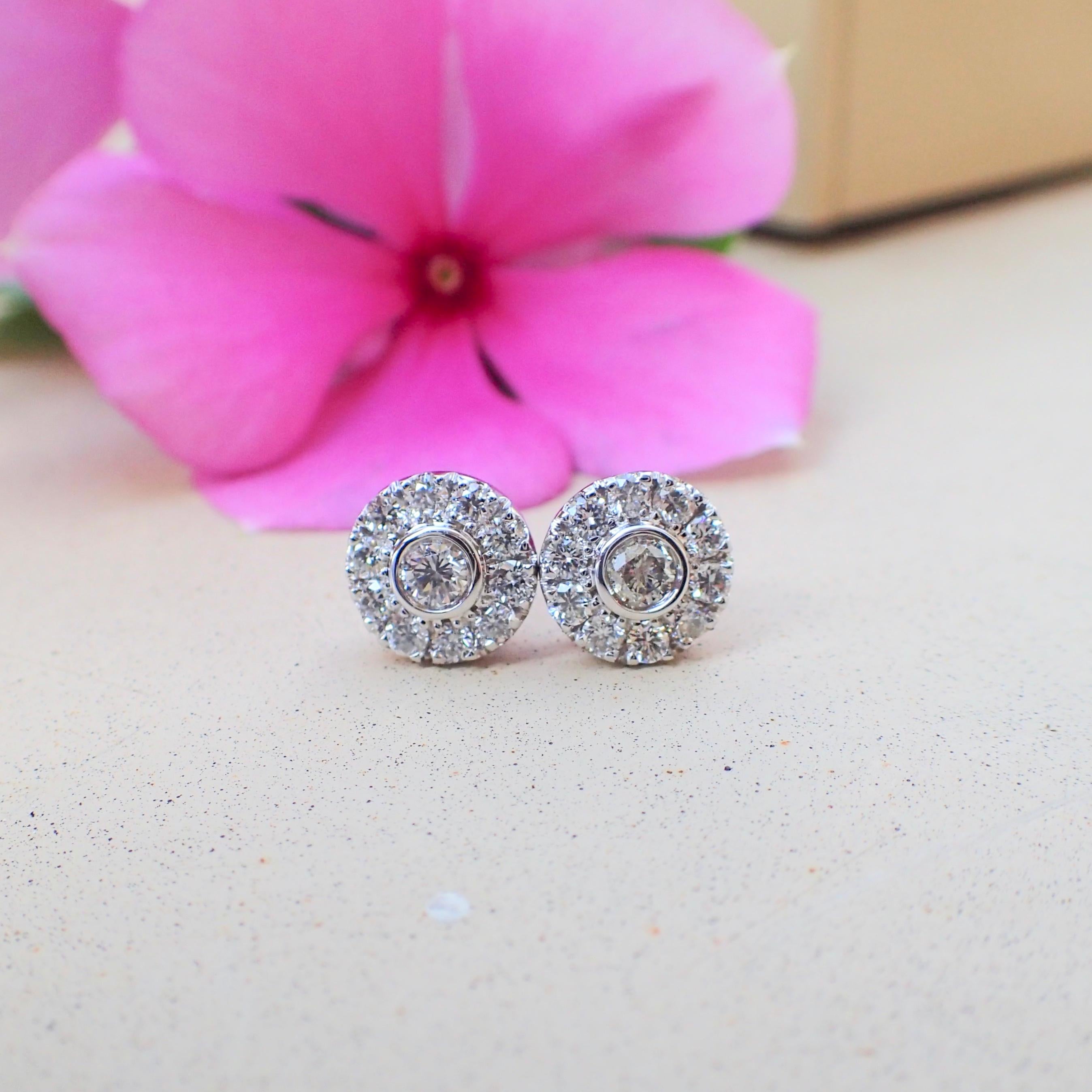 A pair of 18k white gold earrings are bezel set with two (2) Round Brilliant Cut diamonds measuring 2.5mm x 2.5mm that weigh a total of 0.12 carats with Cold Grade G and Clarity Grade VS and surrounding the center stones are twenty (20) prong set