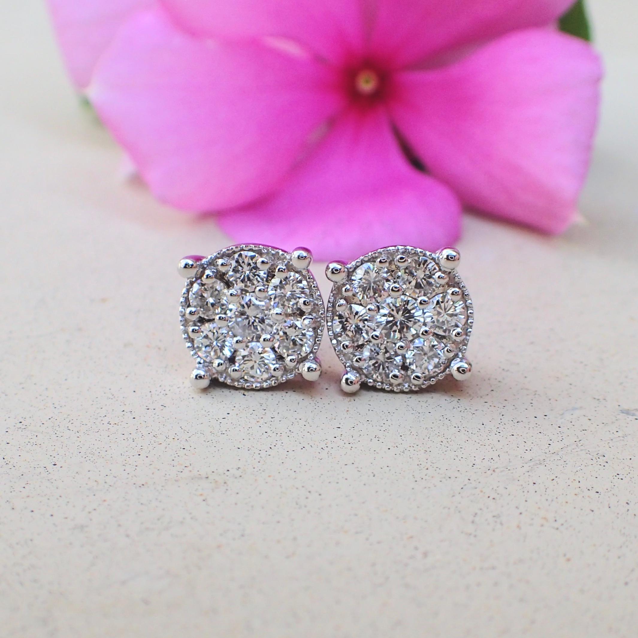 A pair of 18k white gold earrings are prong set with two (2) Round Brilliant Cut diamonds measuring 2.6mm x 2.6mm that weigh a total of 0.16 carats with Cold Grade G and Clarity Grade VS and surrounding the center stones are twelve (12) prong set
