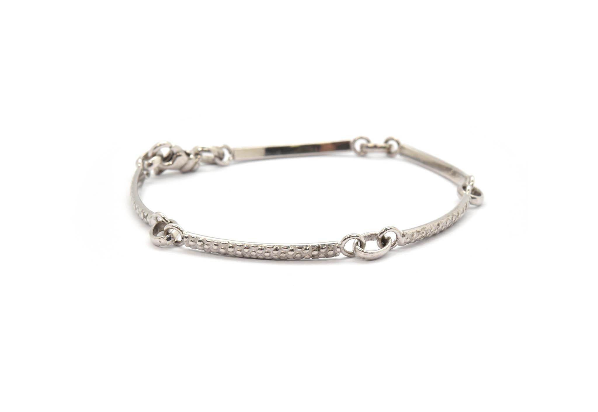 This bracelet is crafted in 18k white gold. It is made of textured links that measure 34mm in length. The bracelet measures 4.5mm at its widest point, and it will fit up to an 8-inch wrist. The bracelet weighs 7.38 grams.
