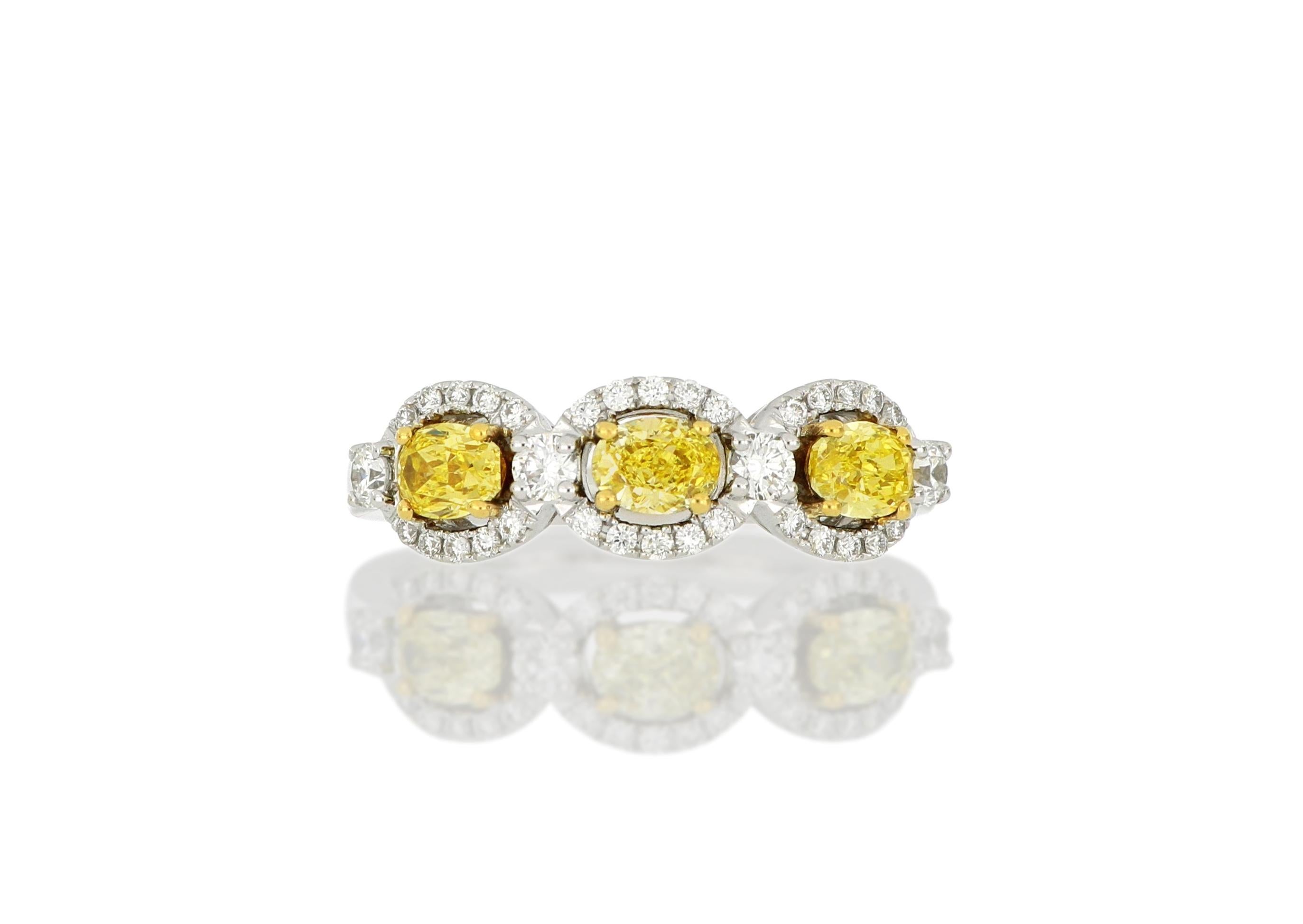 A three-stone yellow diamond ring, set with three oval-shaped natural fancy yellow diamonds weighing approximately 0.69 carats, each within a brilliant-cut white diamond surround,  total weighing approximately 0.32 carats, mounted in 18 Karat white