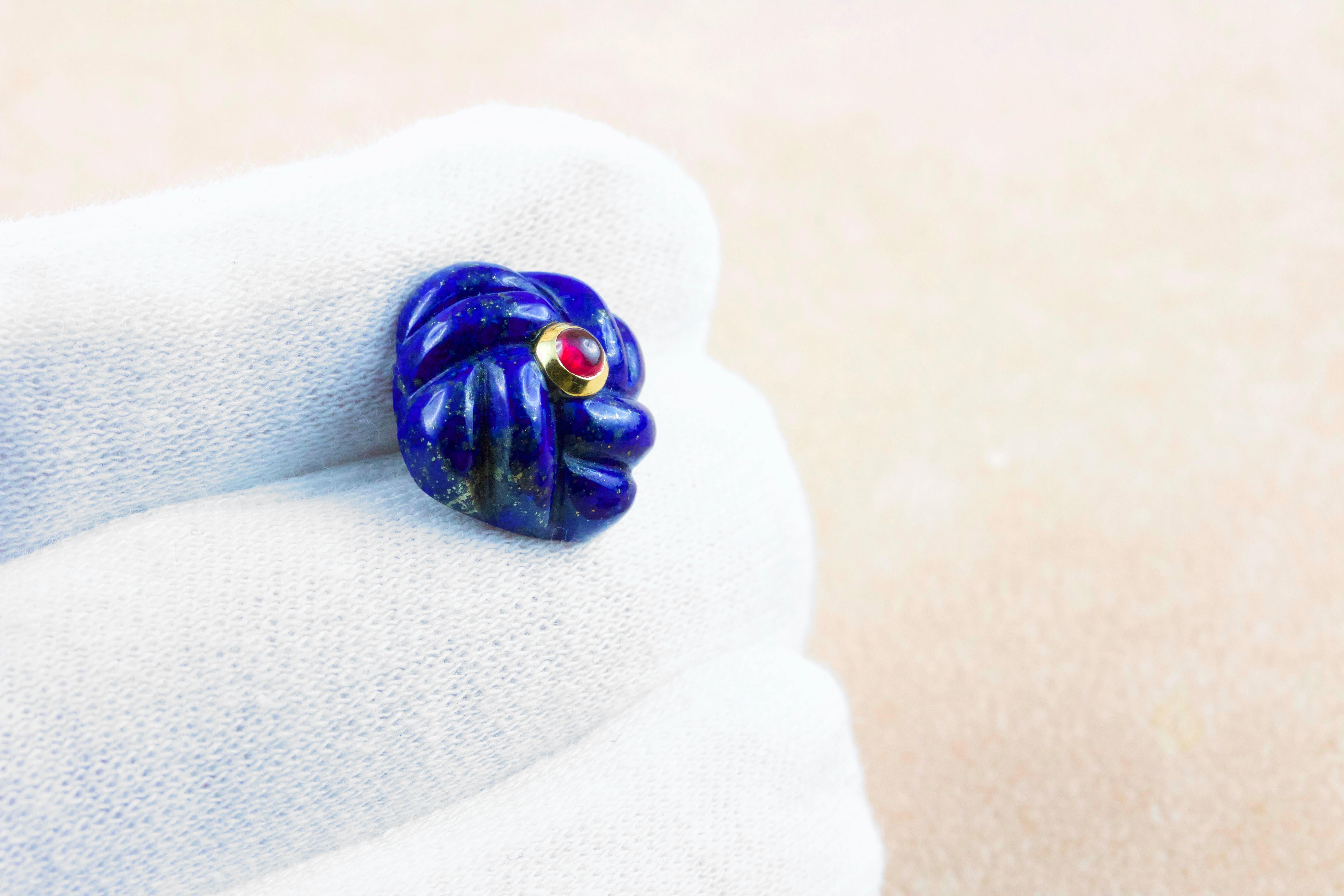 Diese klassischen Manschettenknöpfe sind aus Lapislazuli gefertigt und haben eine quadratische Vorderseite mit einer auffälligen Struktur, die ein verwobenes Gewebe nachahmt.
Die Quadrate sind in der Mitte mit Cabochon-Rubinen verziert. 
Der Knebel