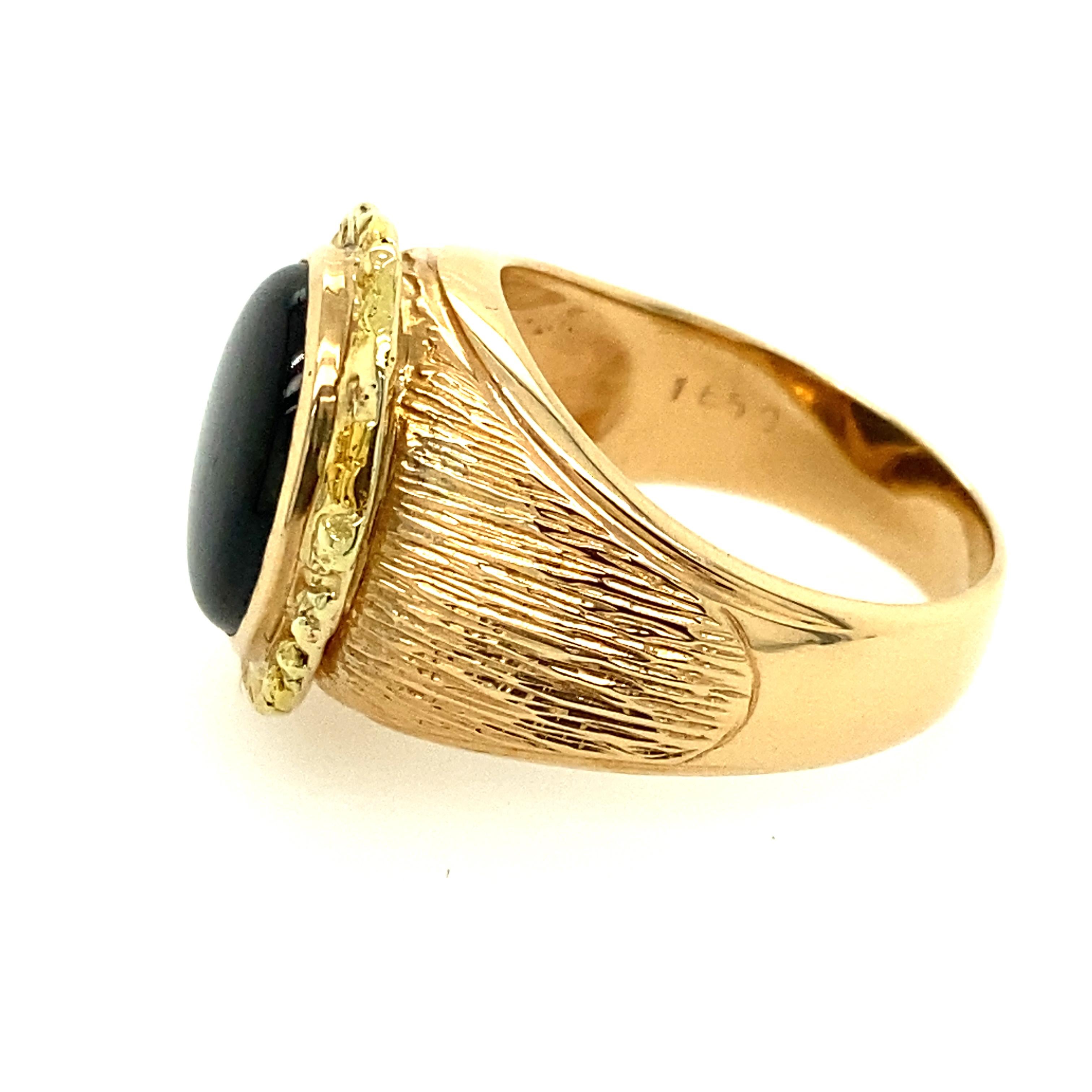 18 Karat Yellow Gold 11.35 Carat Star Sapphire Black Star Ring.

The ring showcase of an oval cabochon cut sapphire black star secured in a bezel setting. Textured patterns on slightly domed shoulders. Slightly half rounded band. Inside band stamped