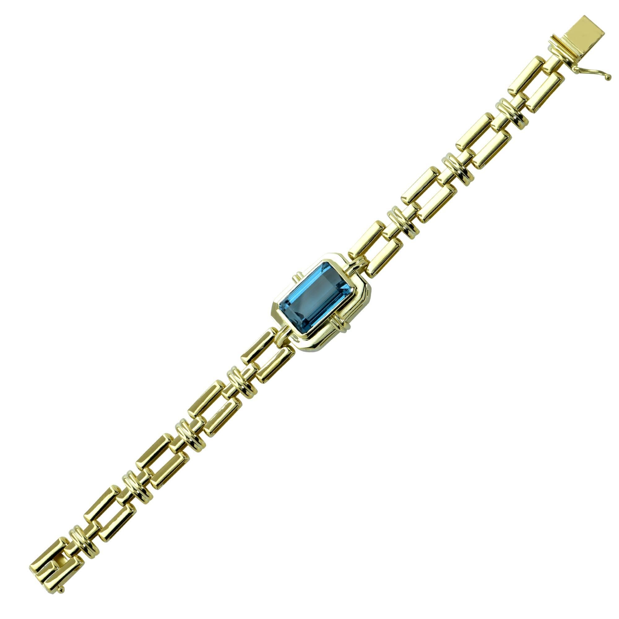 This exotic 18 Karat Yellow Gold link bracelet features a spectacular electric blue emerald cut Topaz weighing approximately 12 carats, framed in 18 karat Yellow Gold. The geometric lines of the links of this bracelet superbly compliment the cut of