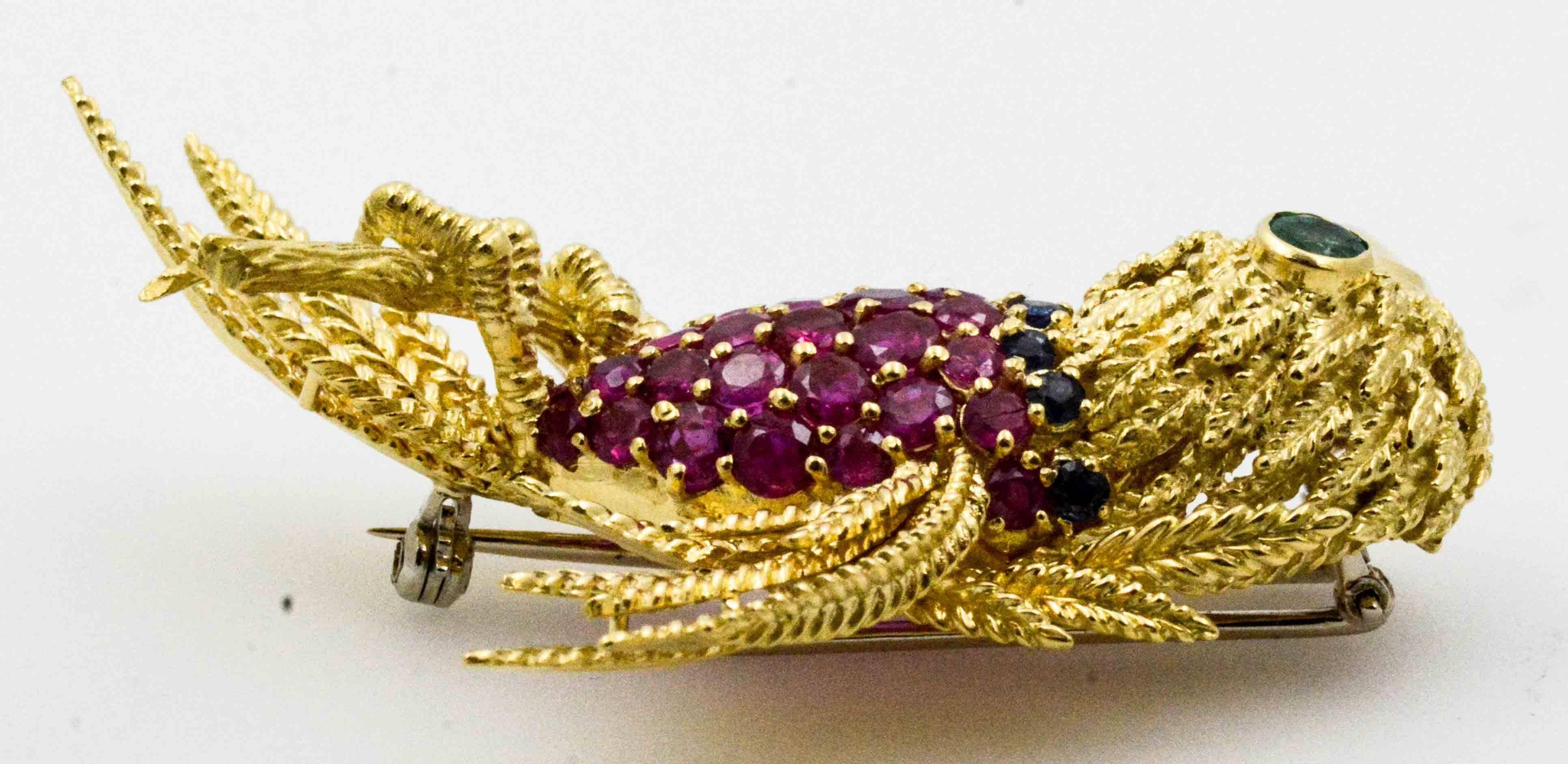 Poised and ready to squawk is an exceptional 18 carat yellow gold parrot brooch. This intricate little bird has a 0.15 carat Emerald eye, a collar of  (8) 0.75 ct round blue sapphires, and a glamorous body of (38) 5.70 ctw round rubies. Expertly