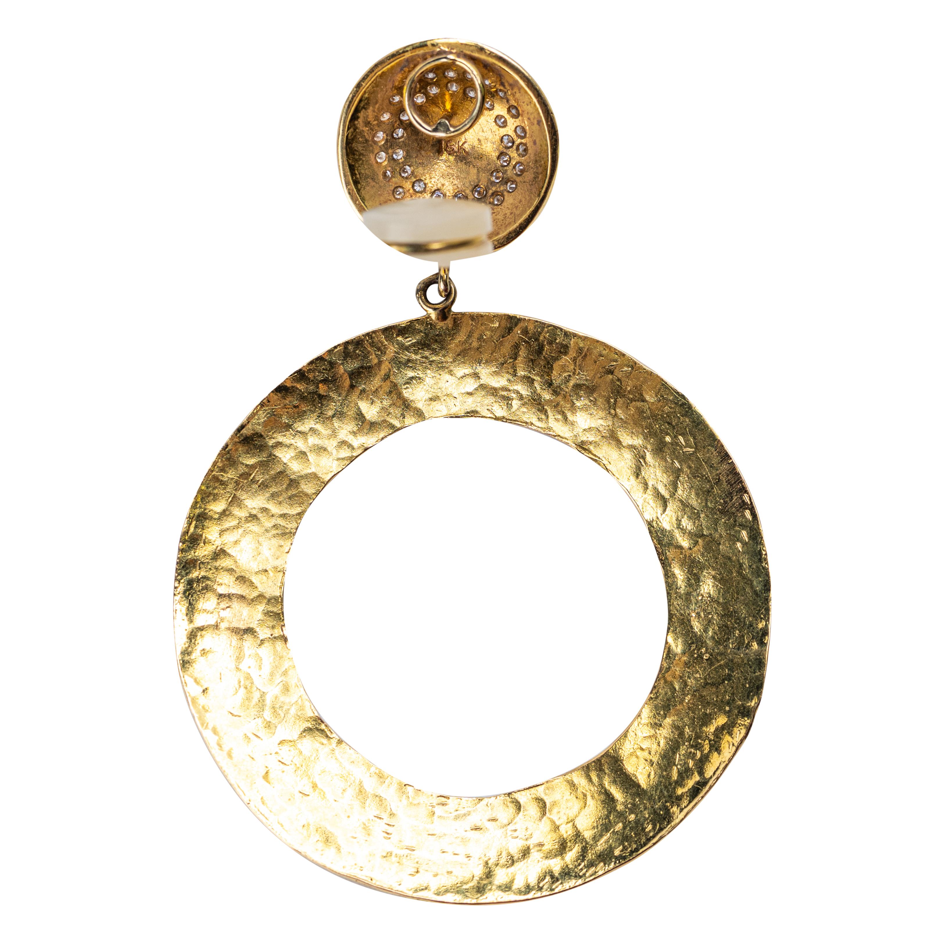 Questi orecchini in oro giallo 18 k. con finitura martellata sono al tempo stesso scultorei e affascinanti. I ciondoli circolari pendono da cupole con pavé di diamanti, ognuna delle quali brilla di raffinate pietre rotonde con taglio a brillante. Il