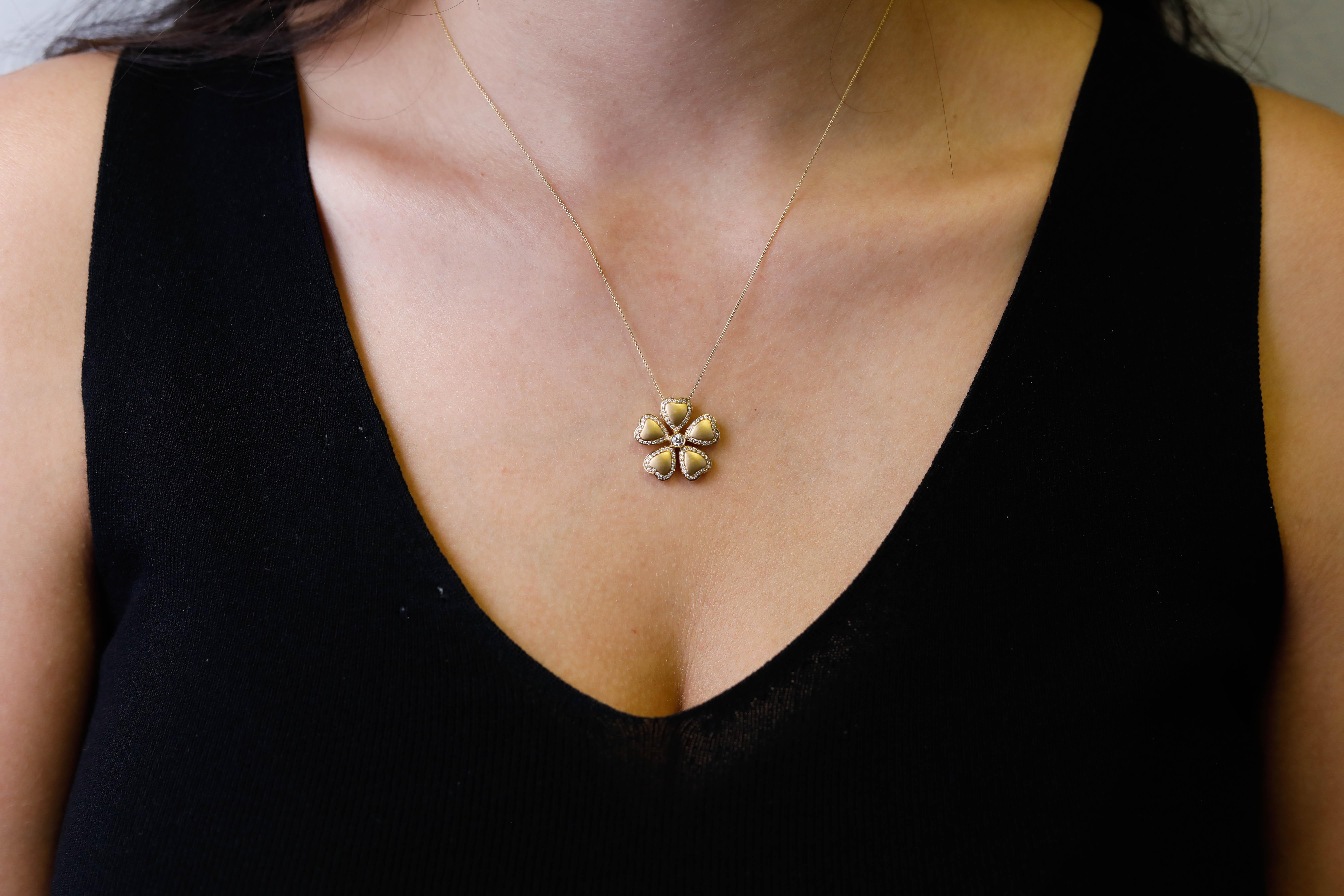 This 18K yellow gold diamond floral pendant necklace makes a feminine statement. The necklace features a unique flower design pendant with a round bezel set diamond in the center and five heart shaped petals edged with sparkling white round