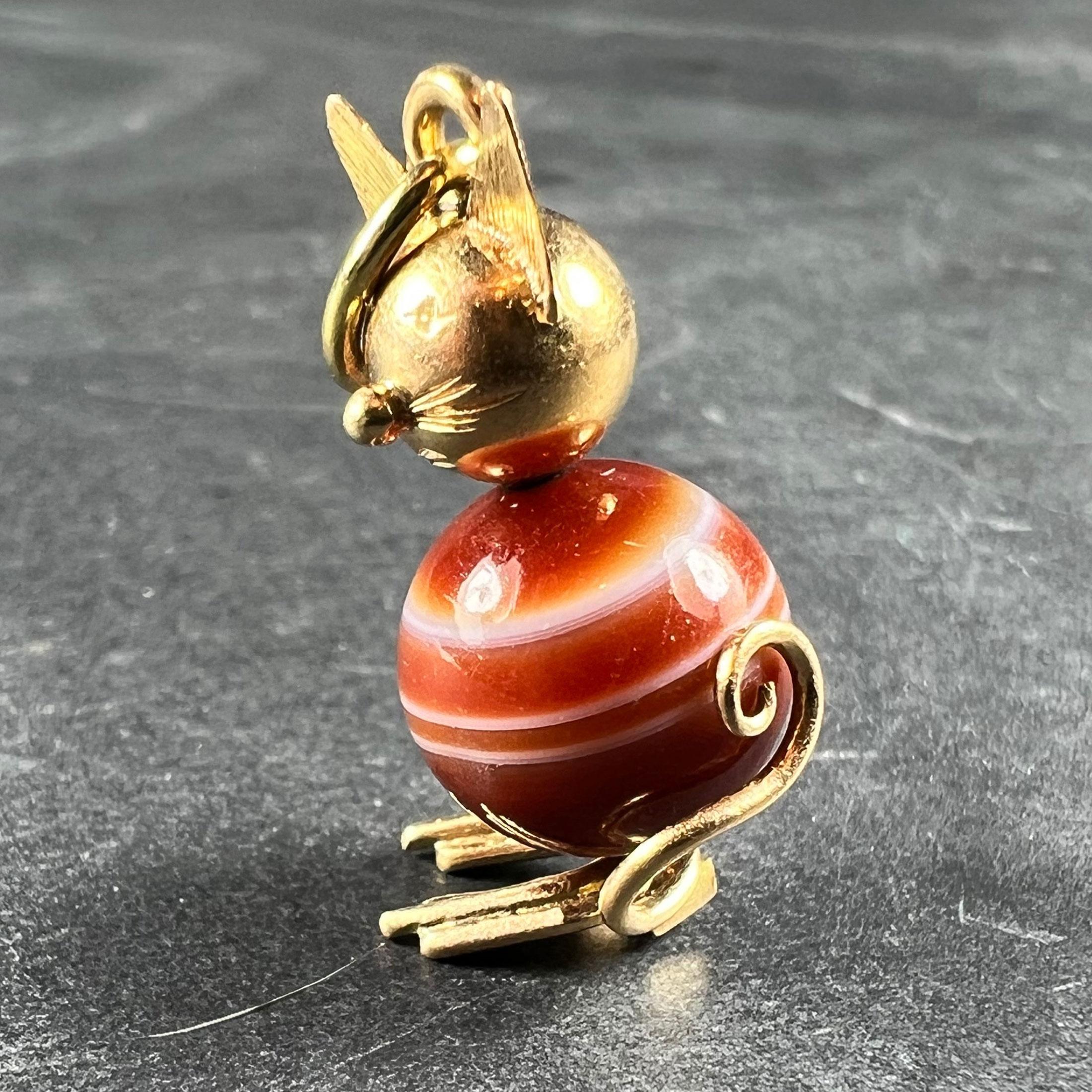 An 18 karat (18K) and banded agate charm pendant designed as a sitting cat. The body is fashioned from a spherical bead of banded brown and white agate, with the head, paws and tail in 18 karat yellow gold. Unmarked but tested as 18