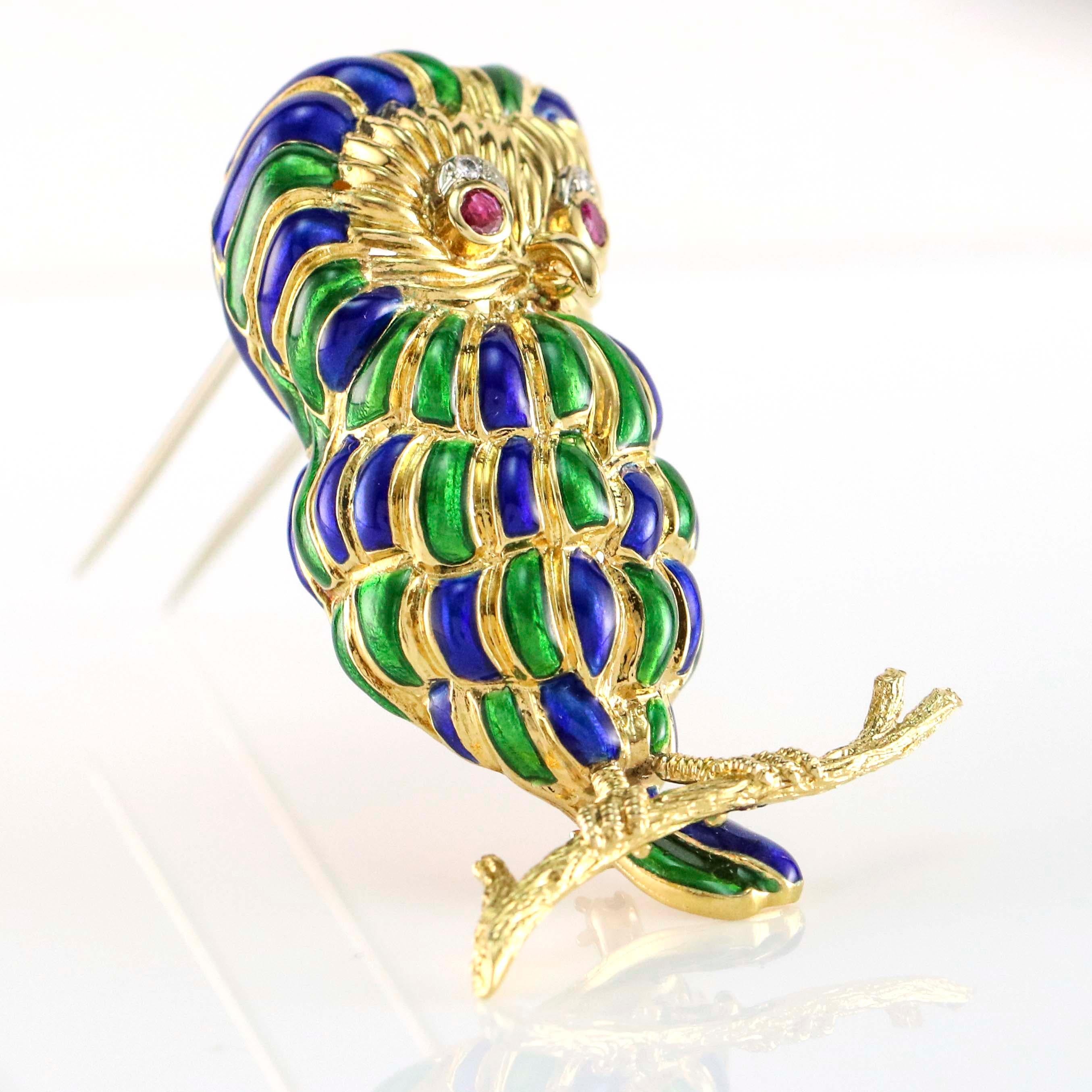 Owl sitting on branch with ruby eyes, blue and green enamel details crafted in 18k yellow gold.