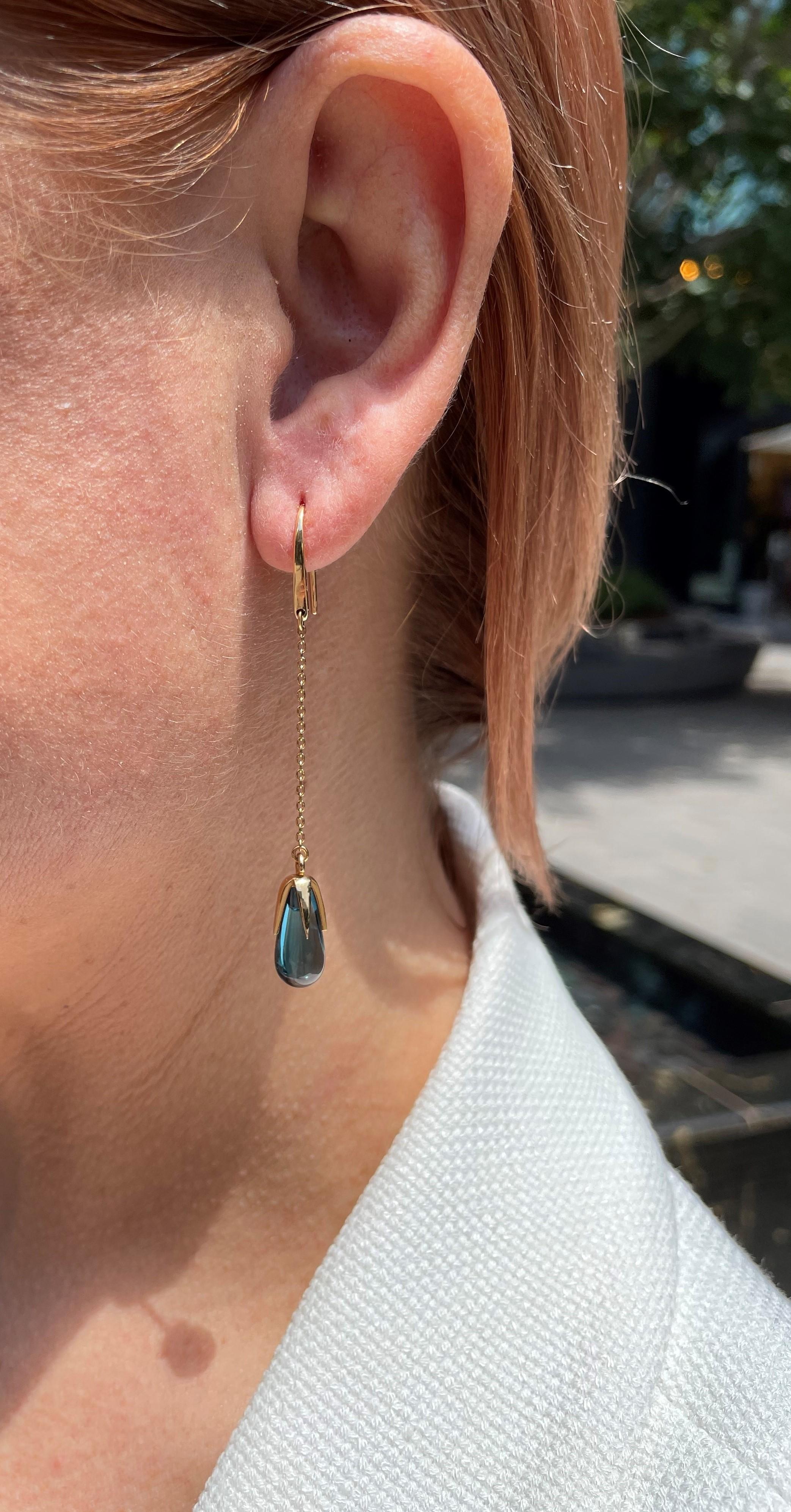 18kt yellow gold and blue topaz drop chandelier earrings. The drop shaped topaz hang from dainty 18kt yellow gold chains and are set in a long four prong setting.