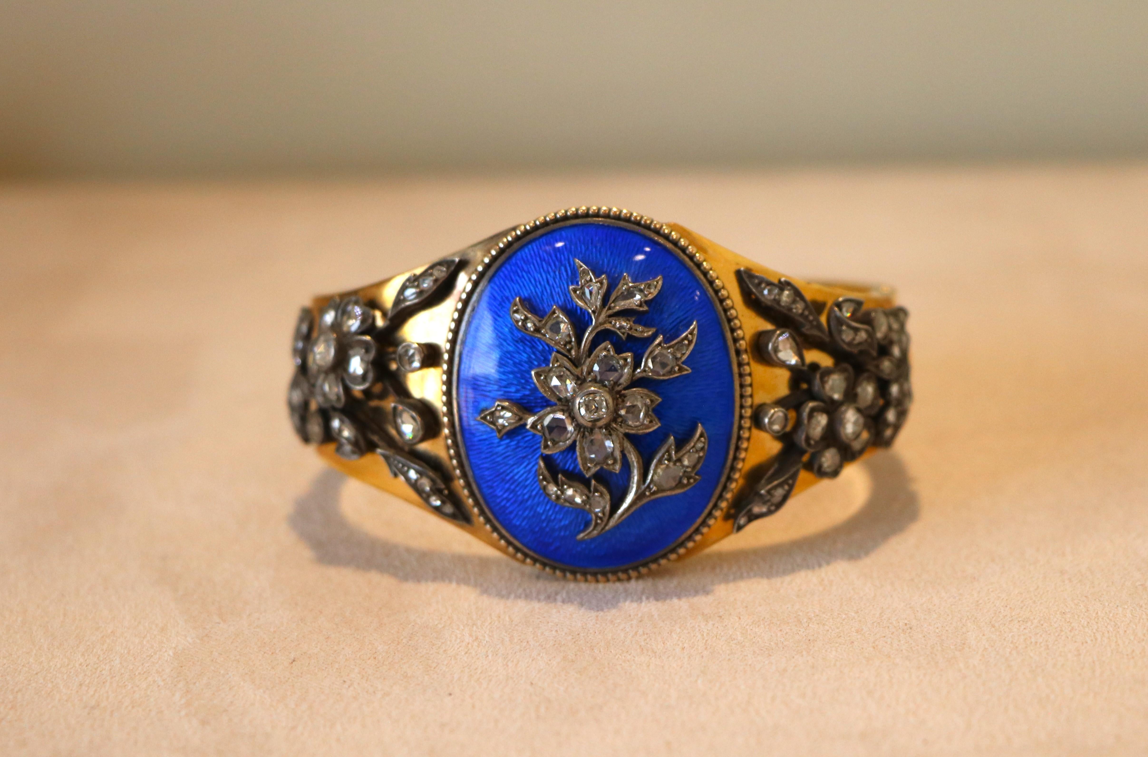 Bracelet rigide de style ancien, en or jaune 18 carats, avec un décor central elliptique recouvert d'émail bleu transparent (émail guilloché).
Au centre du bracelet - un relief en forme de branche florale serti de petits diamants.
Les décorations