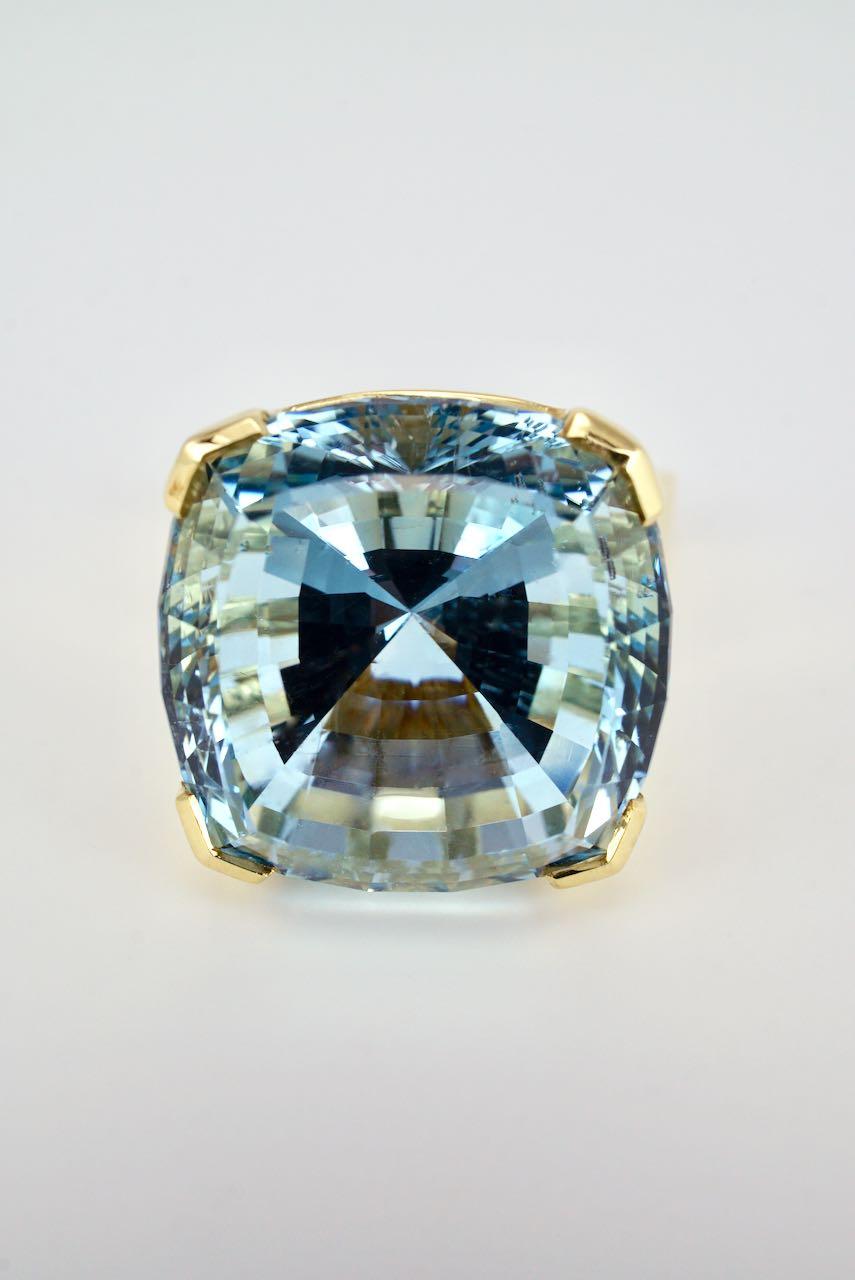 An 18k yellow gold cushion cut blue topaz dress ring featuring an excellent cut topaz of medium blue colour and weighing approx 30cts corner claw set above a tapered shaped shank - a great contemporary design ring that gives a fresh burst of colour