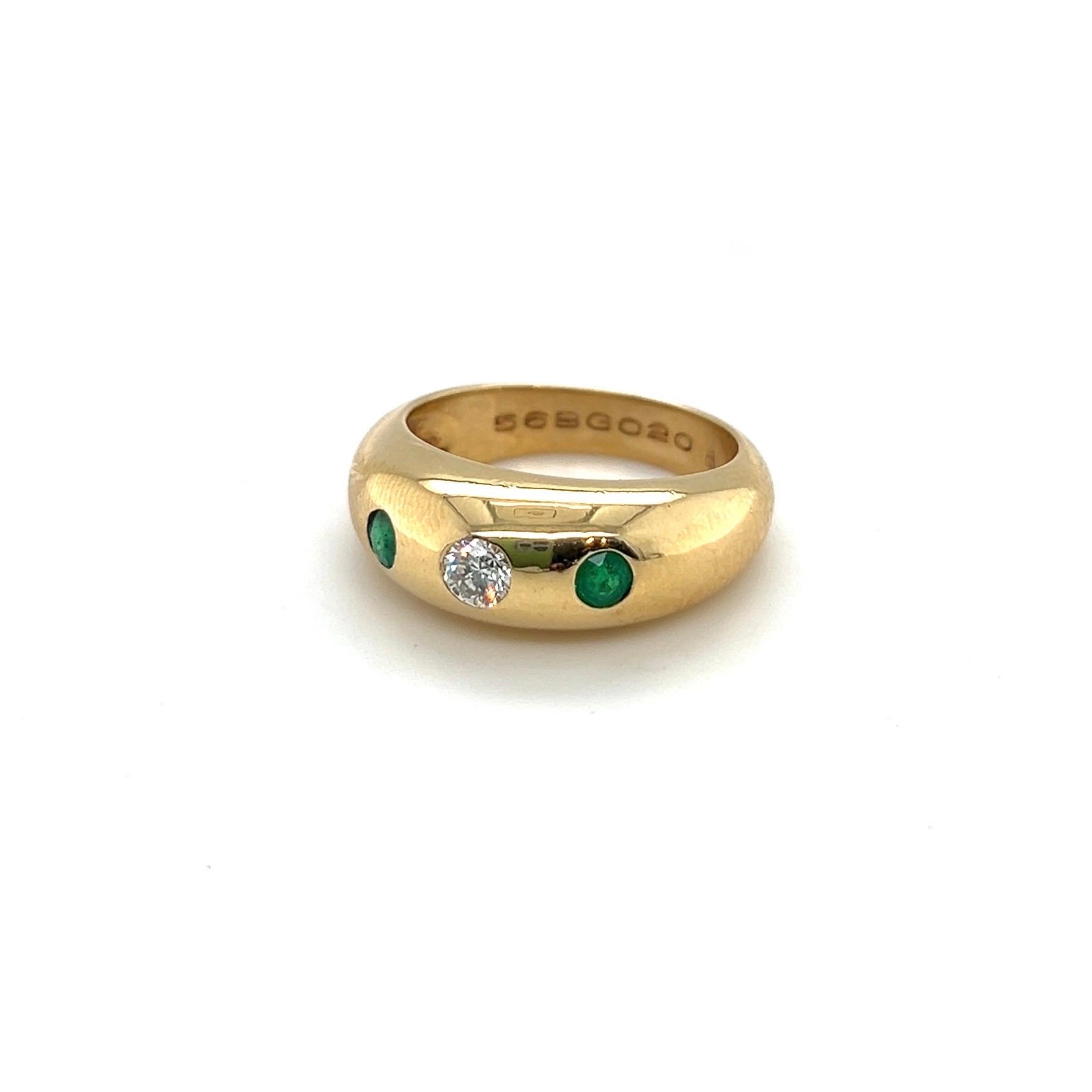 Classic and elegant 18 karat yellow gold, diamond and emerald ring by Cartier, 1980s.

Bandring of slightly domed design, centering upon a brilliant-cut diamond of circa 0.18 carats, flanked by two round emeralds totalling circa 0.15 carats. The