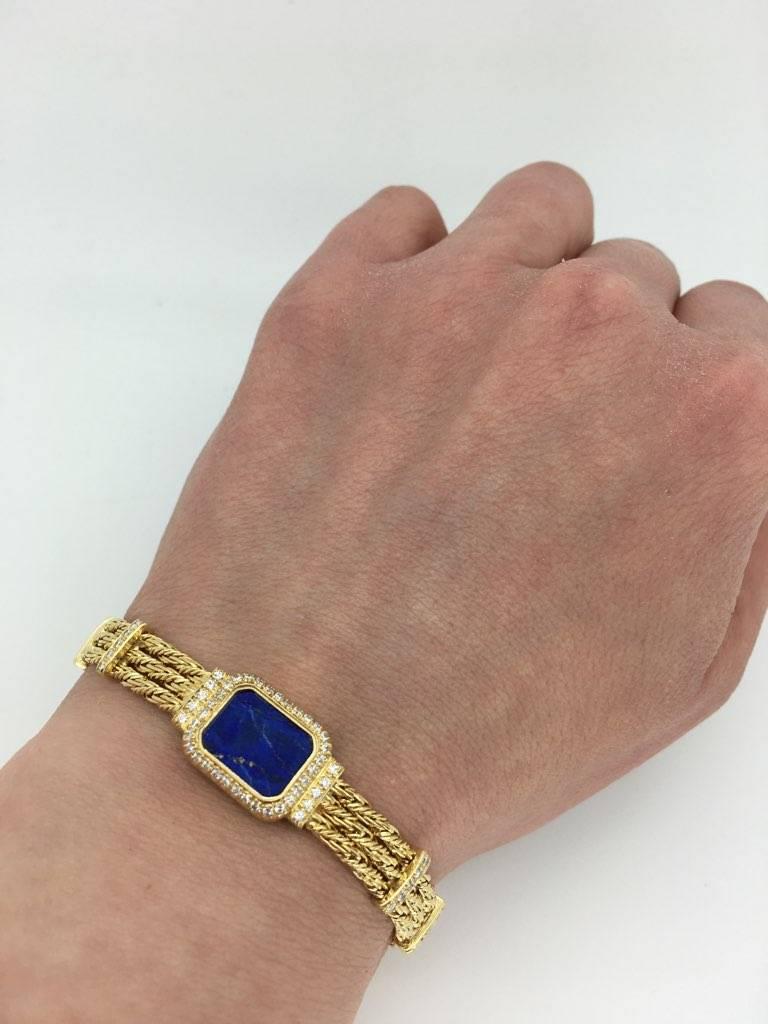 This custom 18K yellow gold Baume & Mercier bracelet was created from a Baume & Mercier watch. The bracelet features an approximately 11.45 x 9.15mm Custom Cut Lapis Lazuli. There are 62 Round Brilliant Cut Diamonds accenting the featured gemstone.