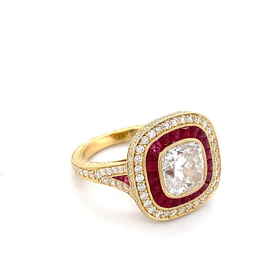 This stunning 18k yellow gold ring has a 3.13ct cushion lab created diamond center stone. The gorgeous center is surrounded by a ruby inner halo and diamond outer halo. The band features a split shank with diamonds half way down and a hand engraved