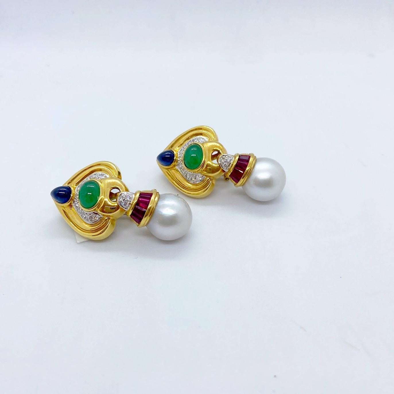 18 karat yellow gold hanging earrings. The top portion of these beautiful earrings are set with a Pear Shaped Cabochon Blue Sapphire and a Oval Cabochon Emerald, along with a row of Round Brilliant Diamonds. A 13mm South Sea Pearl with a Baguette