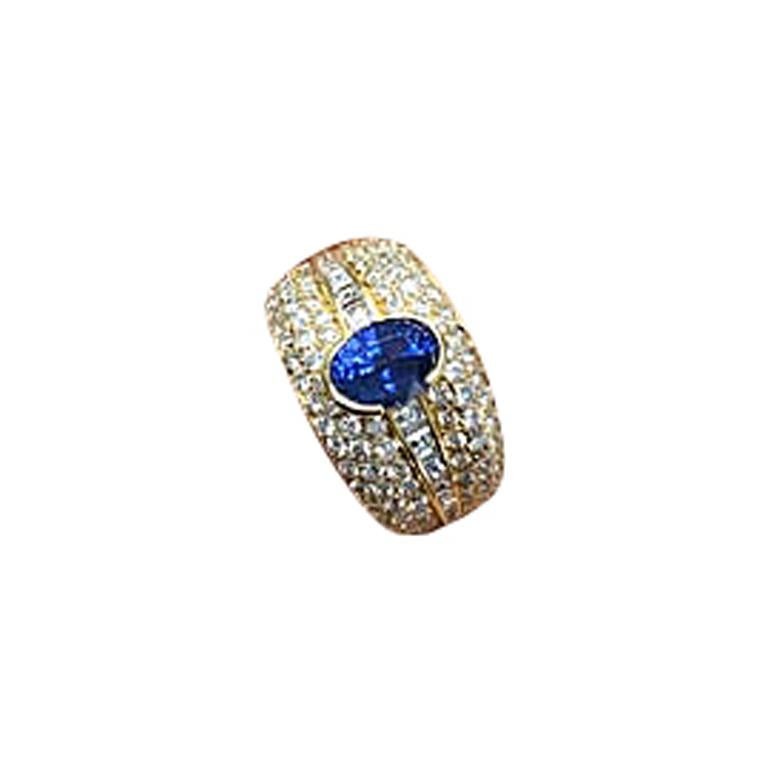 This beautiful 18 karat yellow gold classic style ring features a 1.47 carat oval blue sapphire. The sapphire is bezel set and sits amid round brilliant diamonds. The center of the ring has a row of square and baguette cut diamonds totaling 1.88