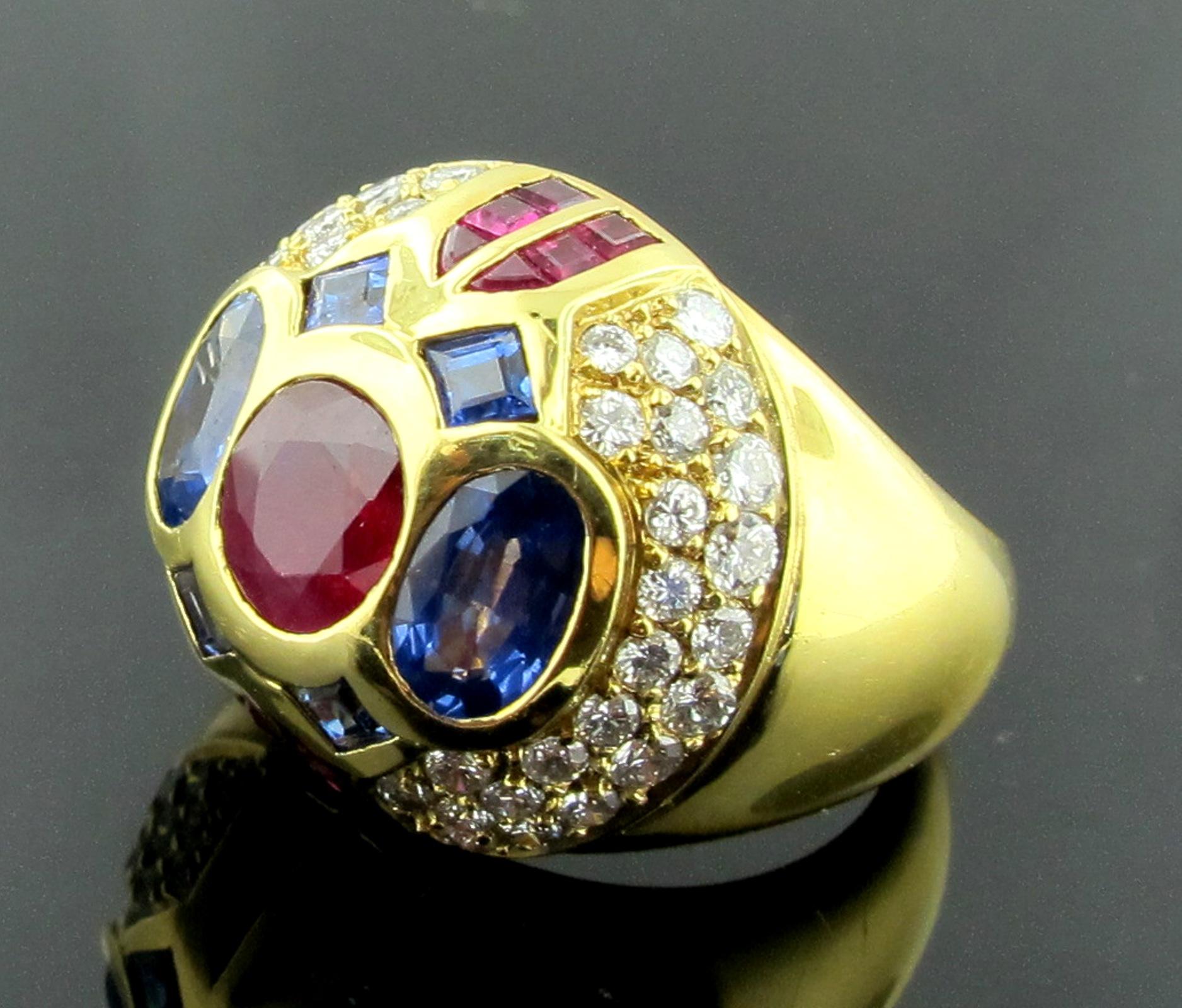 Dome style ring set with a 1.15 carat oval Ruby in the center and includes 2 oval blue Sapphires weighing 1.50 carats, plus 12 calibrated Rubies weighing 0.60 carats; 4 calibrated blue Sapphires weighing 0.40 carats and 46 round brilliant cut