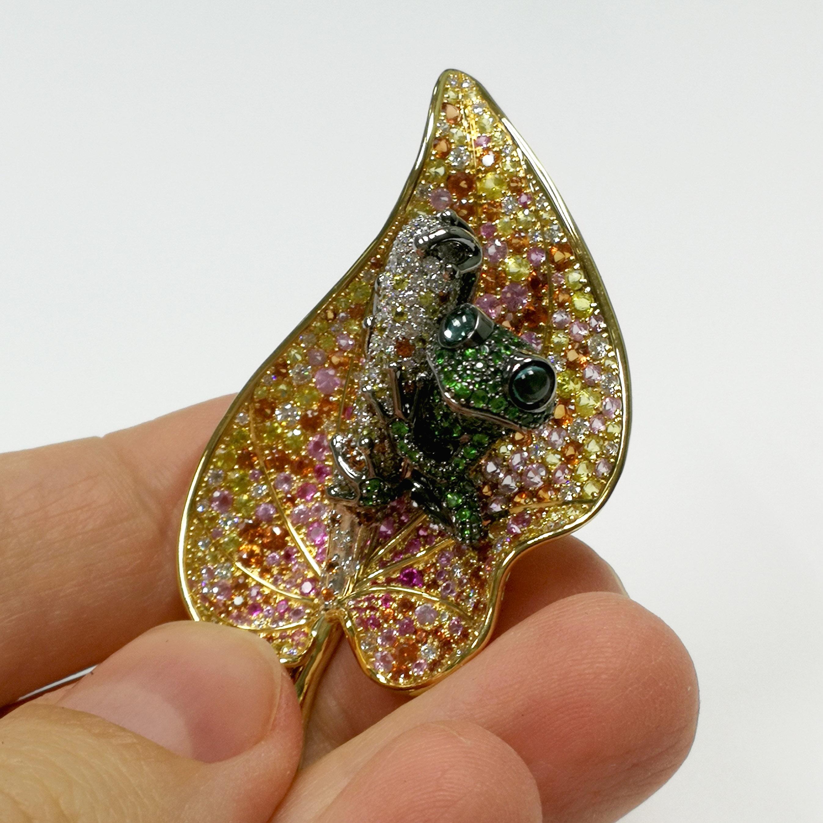 18 Karat Yellow White and Black Gold Frog on the Leaf Brooch. The frog body is all about tsavorites, Leaf are with Diamonds, Pink and Yellow Sapphires

54mm x 32mm x 17mm
18.92 gms