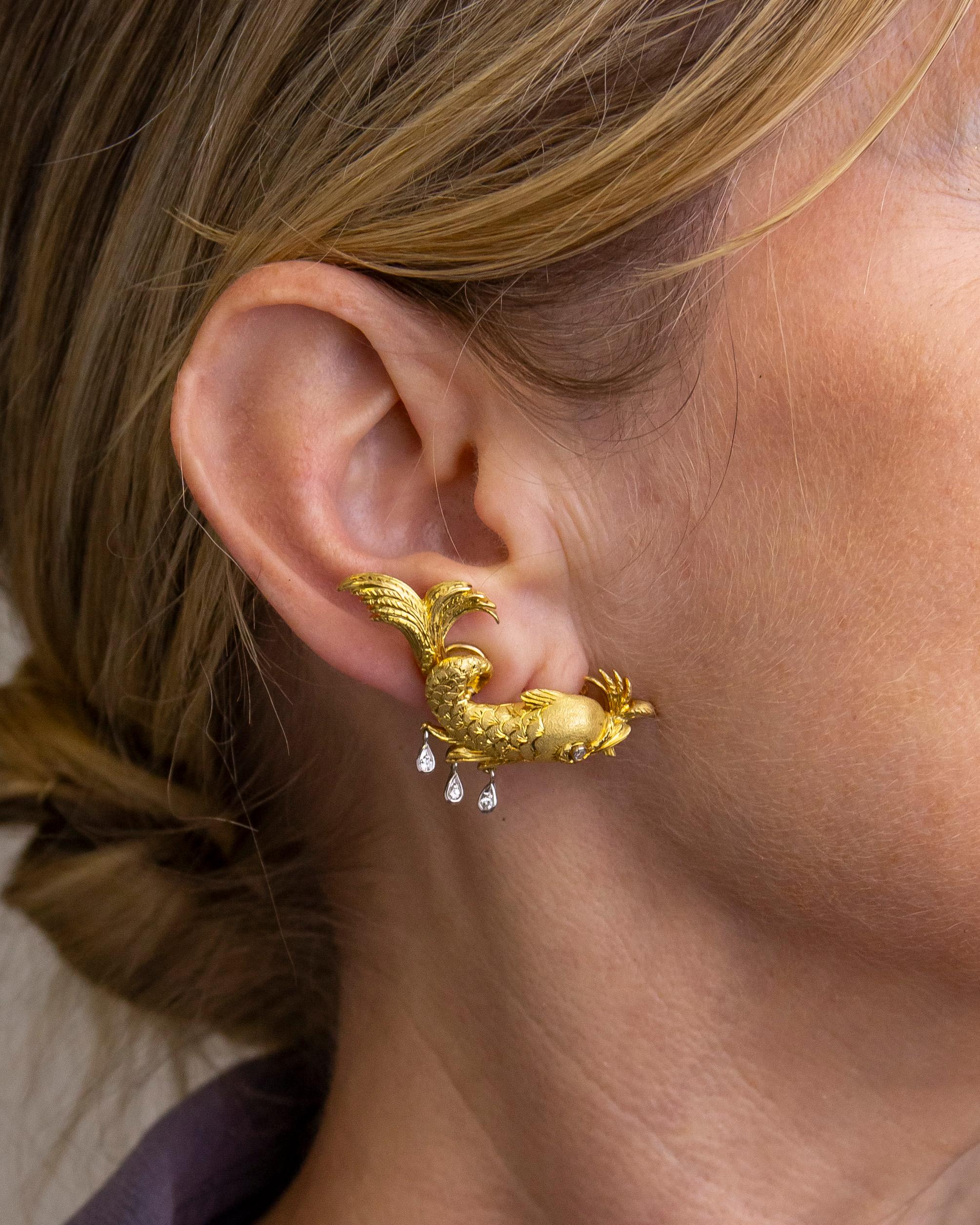 This pair of whimsical ear clips are modelled to depict ancient dolphins as they were rendered in Italian art. Crafted from 18 karat yellow gold, the ear clips are designed to sit at the bottom of the lobe and sweep up the ear. Parts of the body of