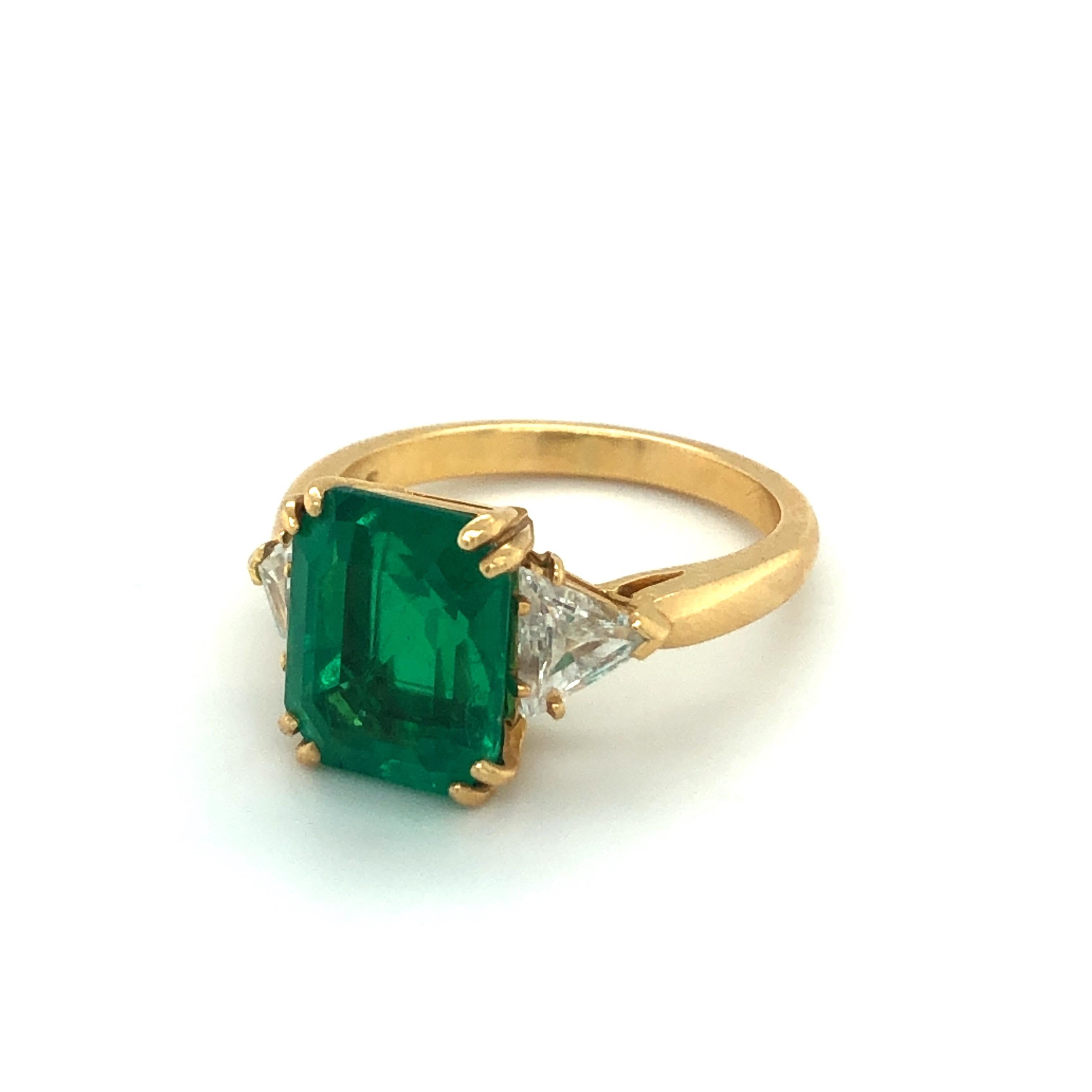 Wonderful 18 karat yellow gold emerald diamond three stone ring by the famous Parisian jewelry house Boucheron.
This classic three stone ring is set with a vivid, evenly colored Colombian emerald of 3.89 carats sided by two triangular diamonds