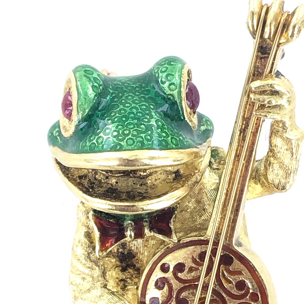Adorable green enamel and ruby 18 karat gold frog brooch. The frog is playing the banjo, and dancing along. The pin measures 40 x 55mm, and is signed Cooper 18k. 