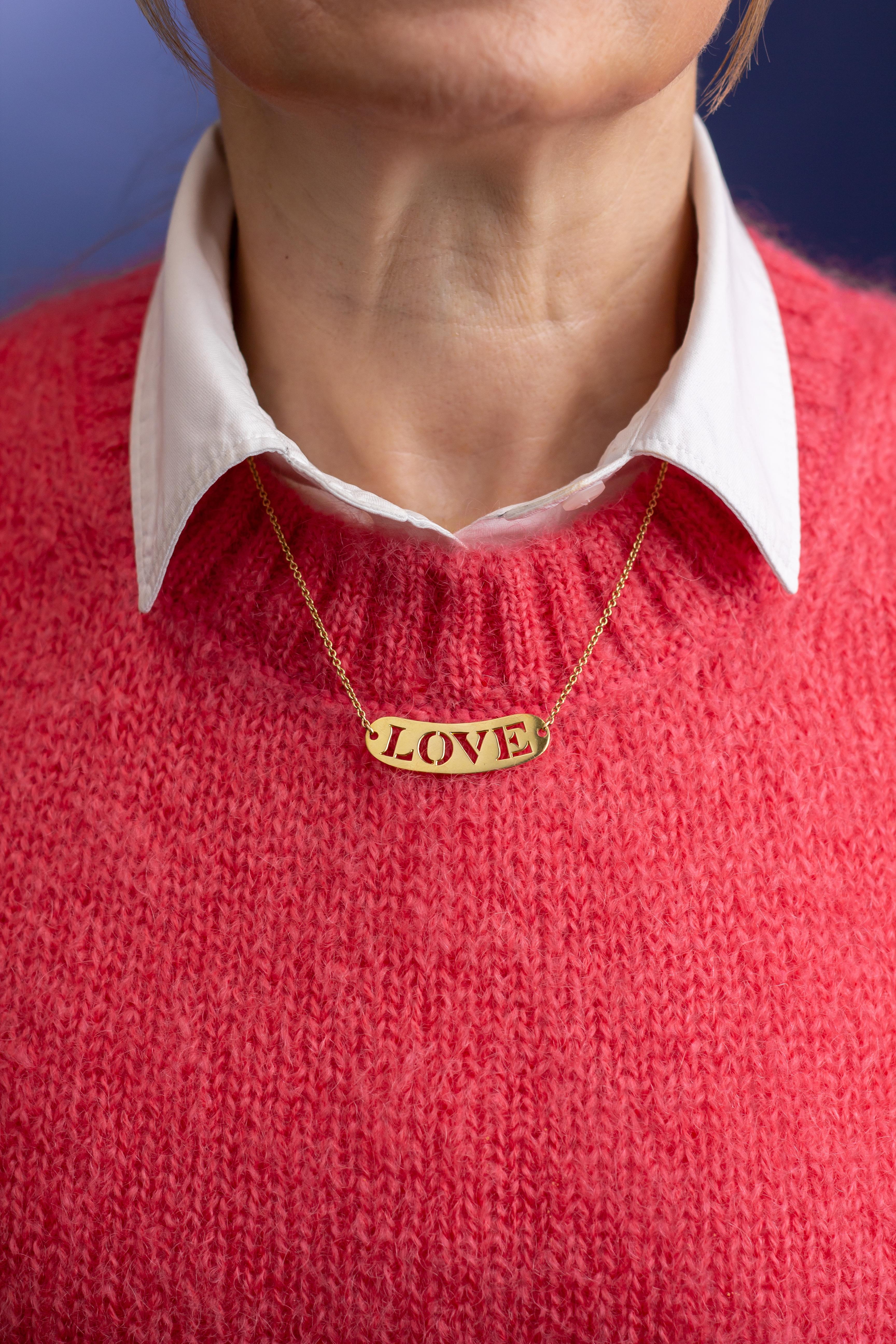 This sweet French necklace features a central plaque spelling 'love' and has been crafted from 18 karat yellow gold. The fine chain necklace centres on an oval yellow gold plaque that has been pierced to reveal the word 'love' which makes it a