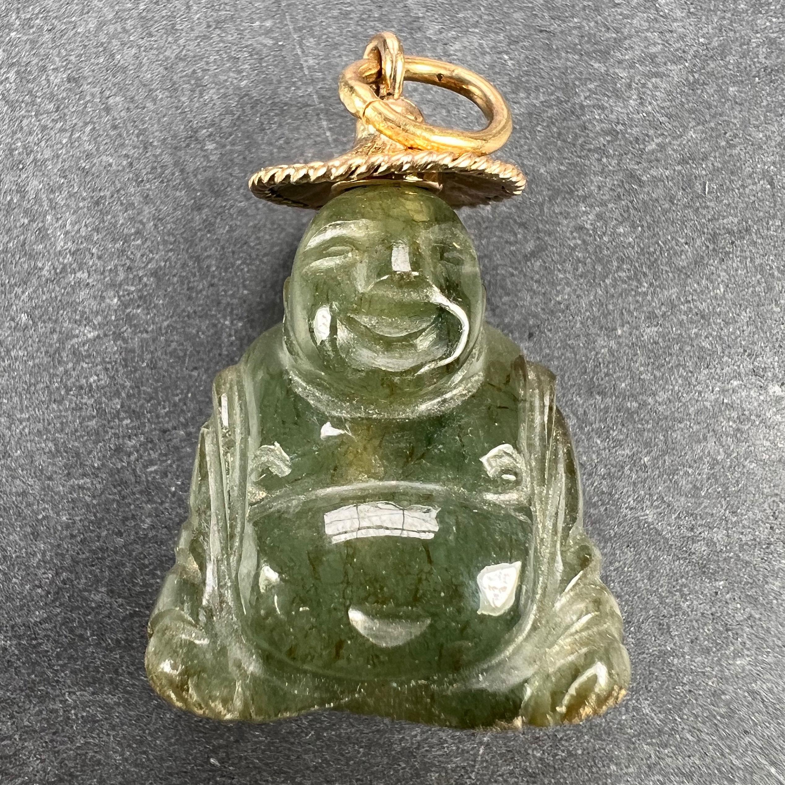 A charm pendant designed as a large carved Buddha sculpture in green jadeite jade with 18 karat (18K) yellow gold terminals. The jadeite is natural, has not been dyed and shows some evidence of natural iron staining. Unmarked but tested for 18 karat