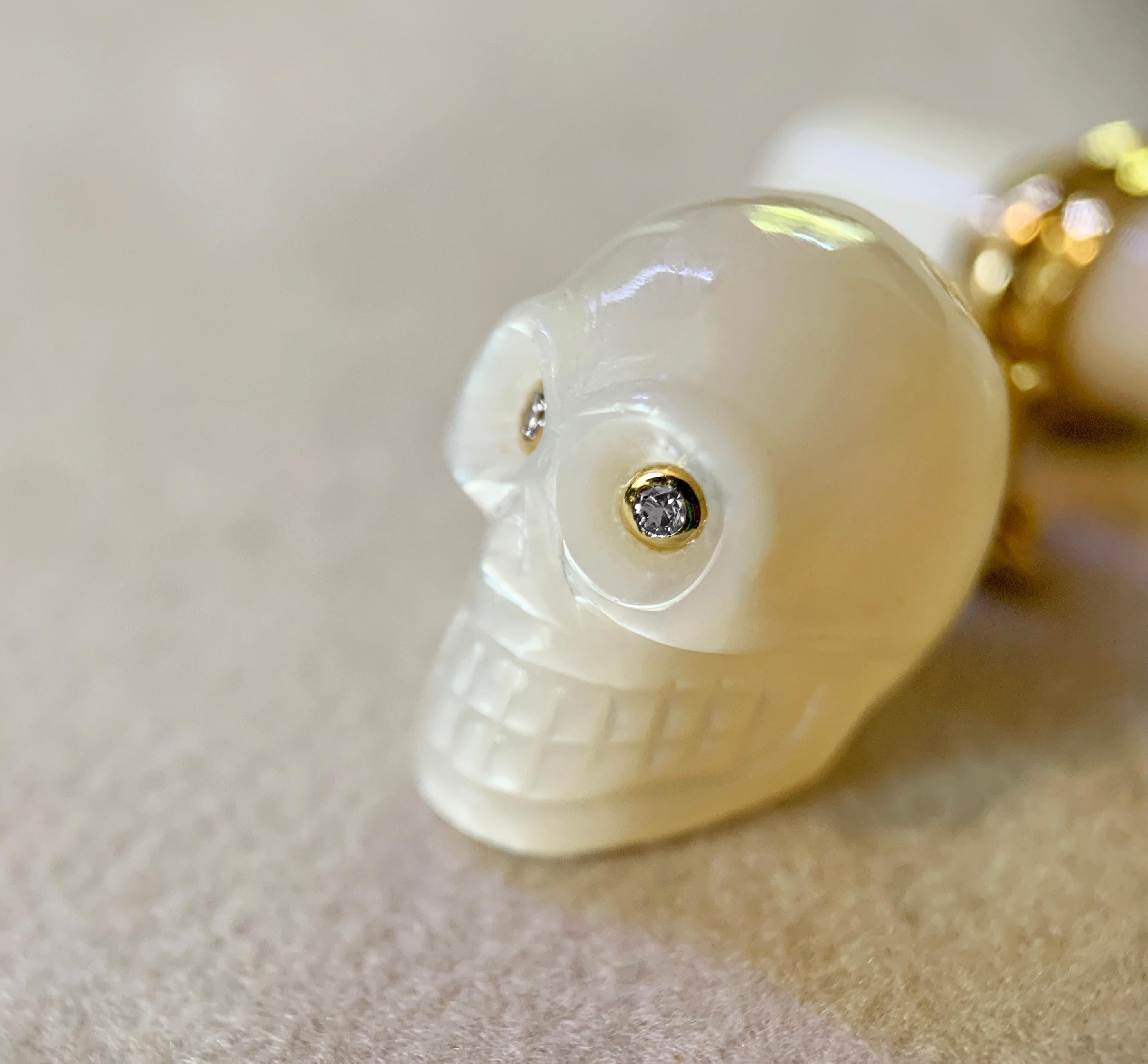 Ces boutons de manchette ludiques sont entièrement réalisés en nacre. La face avant est magistralement sculptée pour représenter un crâne au large sourire et aux orbites enfoncées d'où brillent deux diamants. 
Un poteau en or jaune 18 carats relie