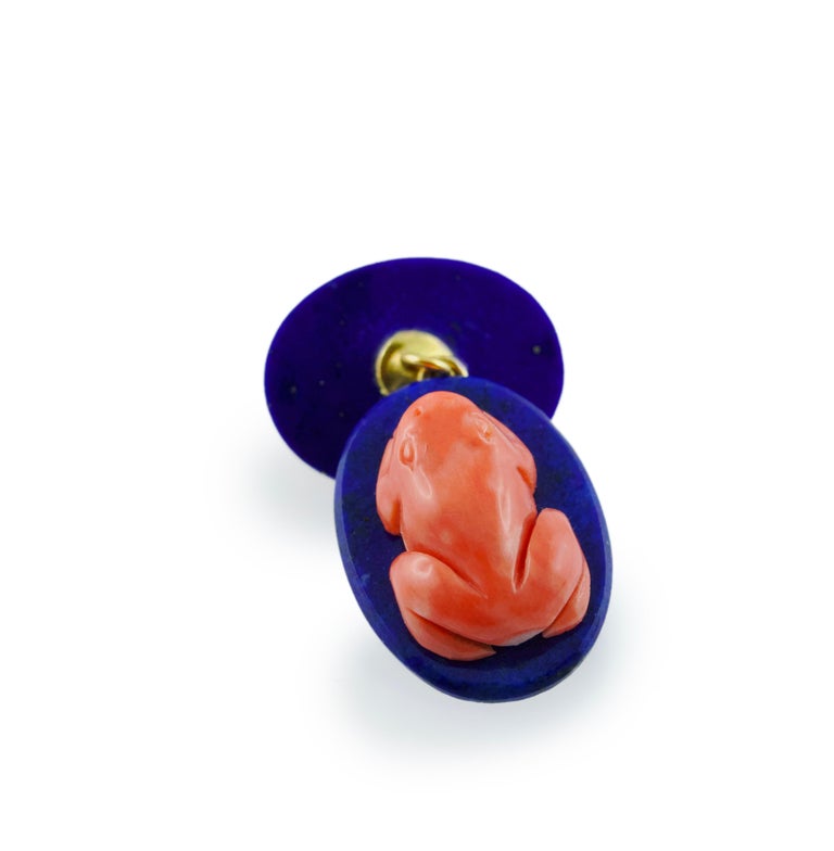 In this striking pair of cufflinks, front face and toggle are identical and feature the body of a small frog vividly depicted and made of Mediterranean coral, resting on an oval base made of lapis lazuli. 
Mounting in 18 karat yellow