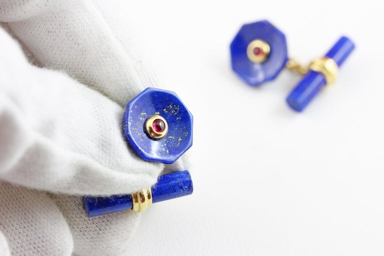 This elegant pair of cufflinks made in lapis lazuli  features a cylindrical toggle and a front face shaped as an octagon with a convex, multifaceted surface and a central ornament made of a ruby cabochon. 
The post linking front face and toggle and