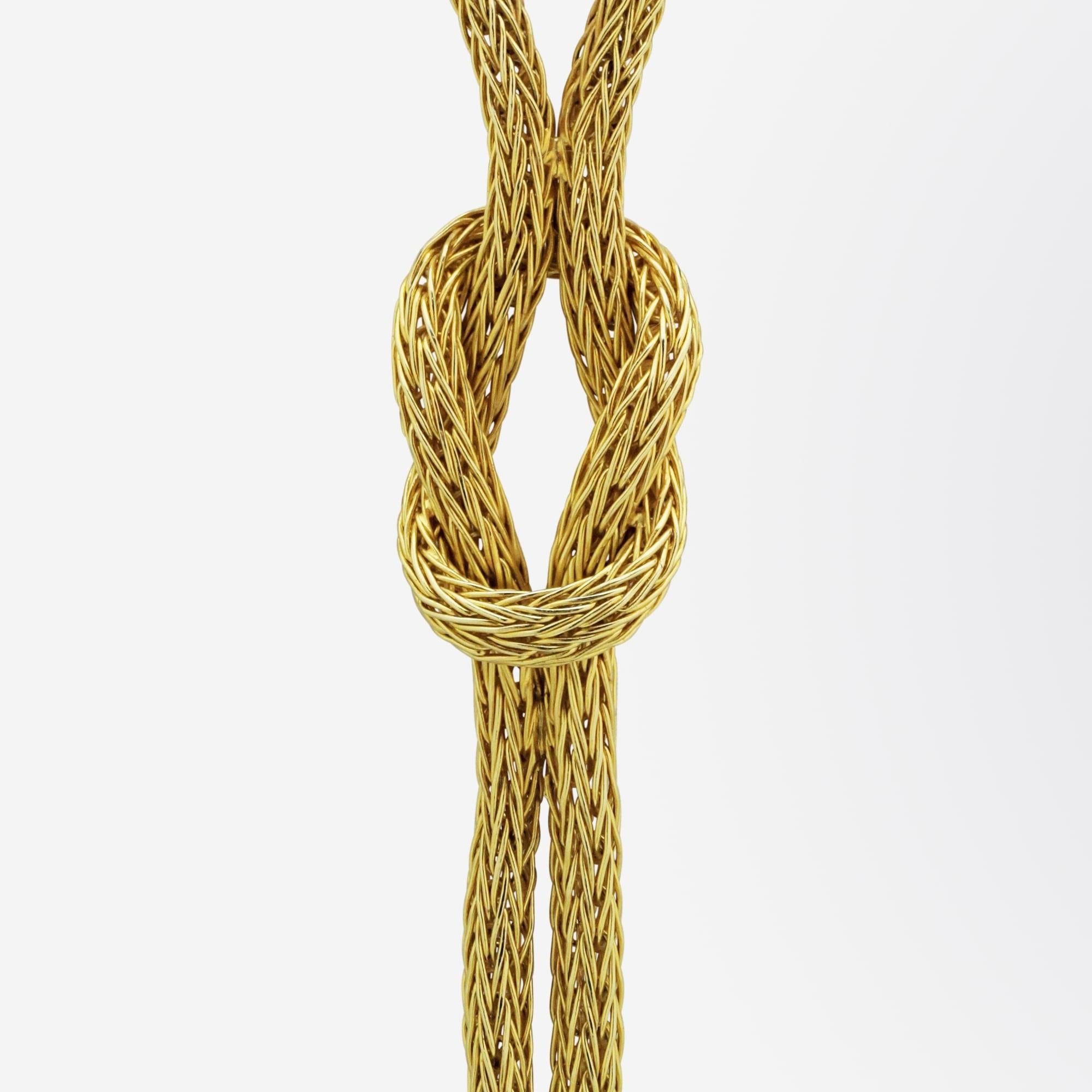 An exceptional lariat style necklace in solid 18 karat yellow gold. The necklace has been manufactured of woven 18 karat yellow gold 'rope' which centres on a 'lovers knot' drop from which hang two Etruscan Revival pendants with tassels. The weave