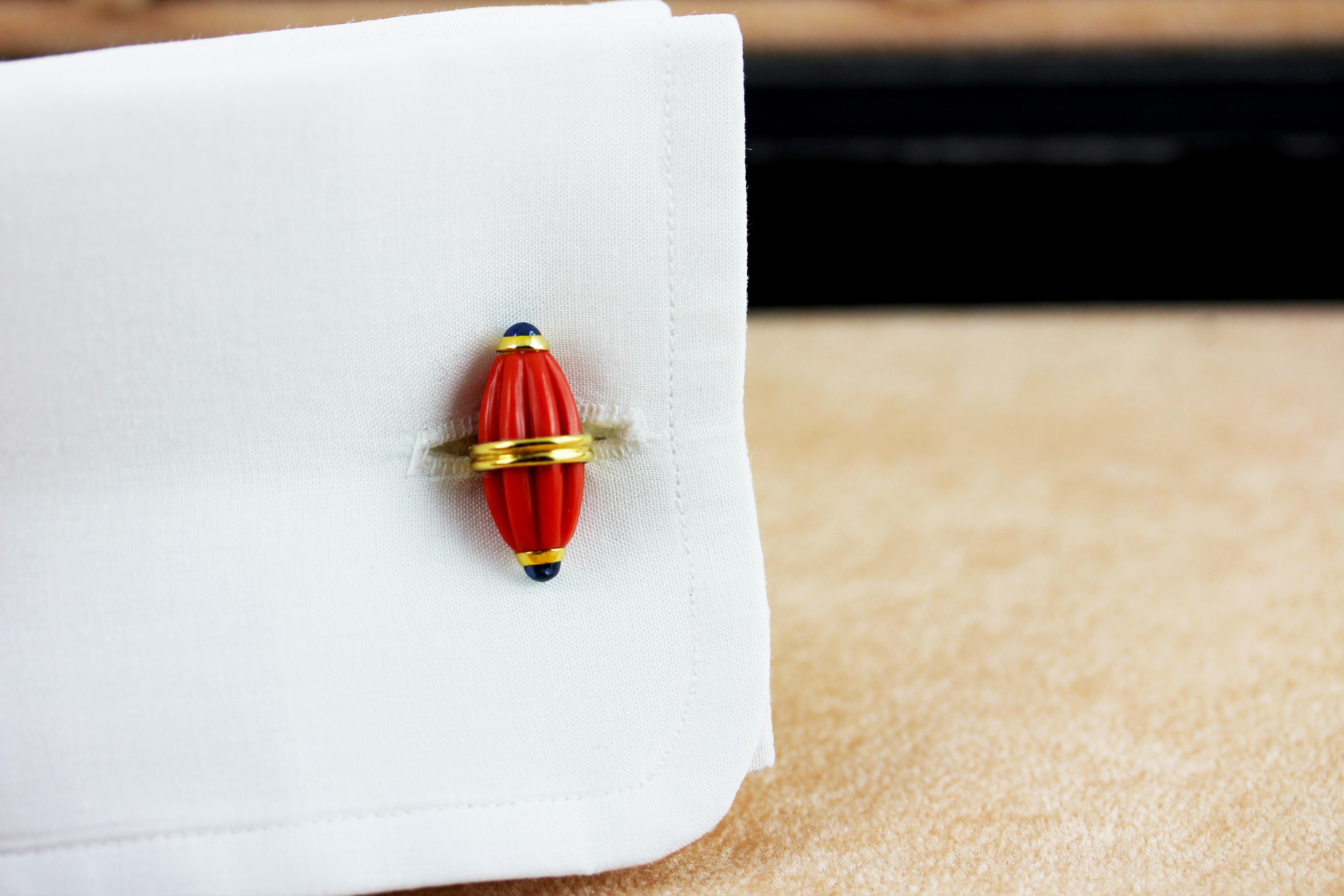 These striking cufflinks feature identical front face and toggle whose oval shapes evokes the silhouette of a barrel, carved with grooves that add dynamism to their texture. 
They are made of Mediterranean coral, adorned with cabochon sapphires at