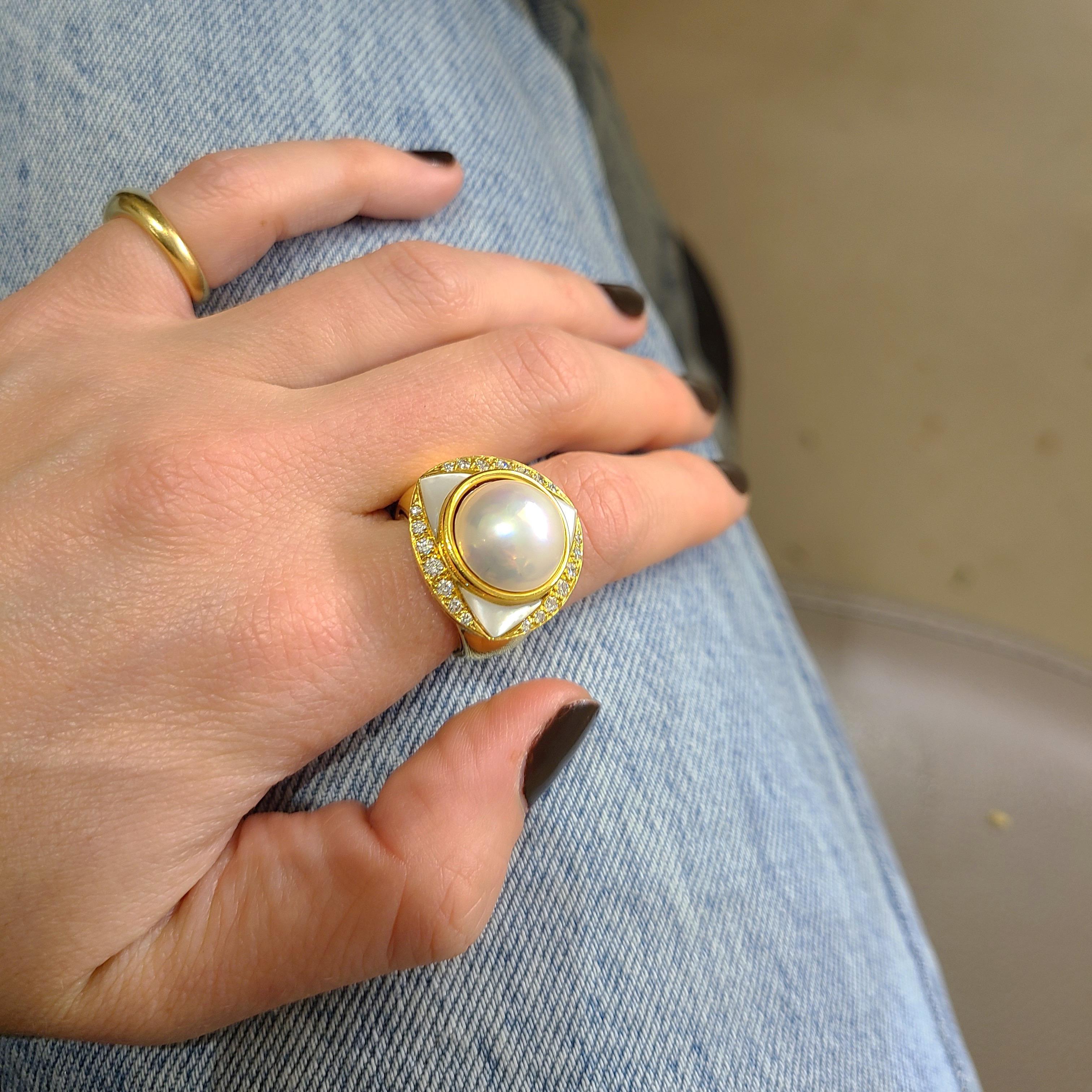 Classic and elegant best describes this 18 karat yellow gold ring. The ring centers a mabe pearl in a bezel setting. Three mother of pearl triangles along with 0.53 carats of round brilliant diamonds surround the central pearl.
Stamped 750 with the