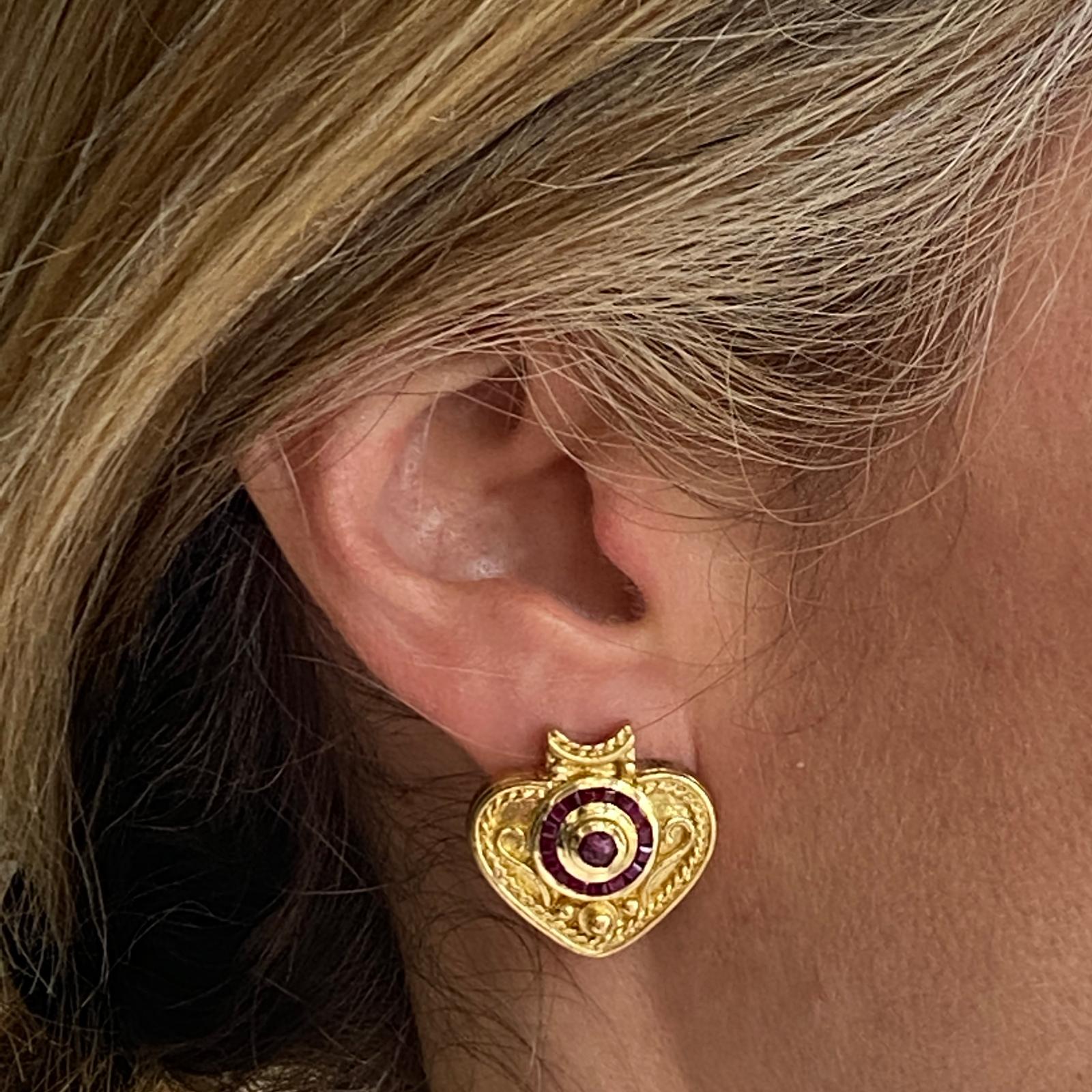 Etruscan style heart earrings fashioned in 18 karat yellow gold. The earrings feature square cut and cabochon natural ruby gemstones set in an Etruscan style gold design featuring scroll and interlocking circle designs with bead spacers. The
