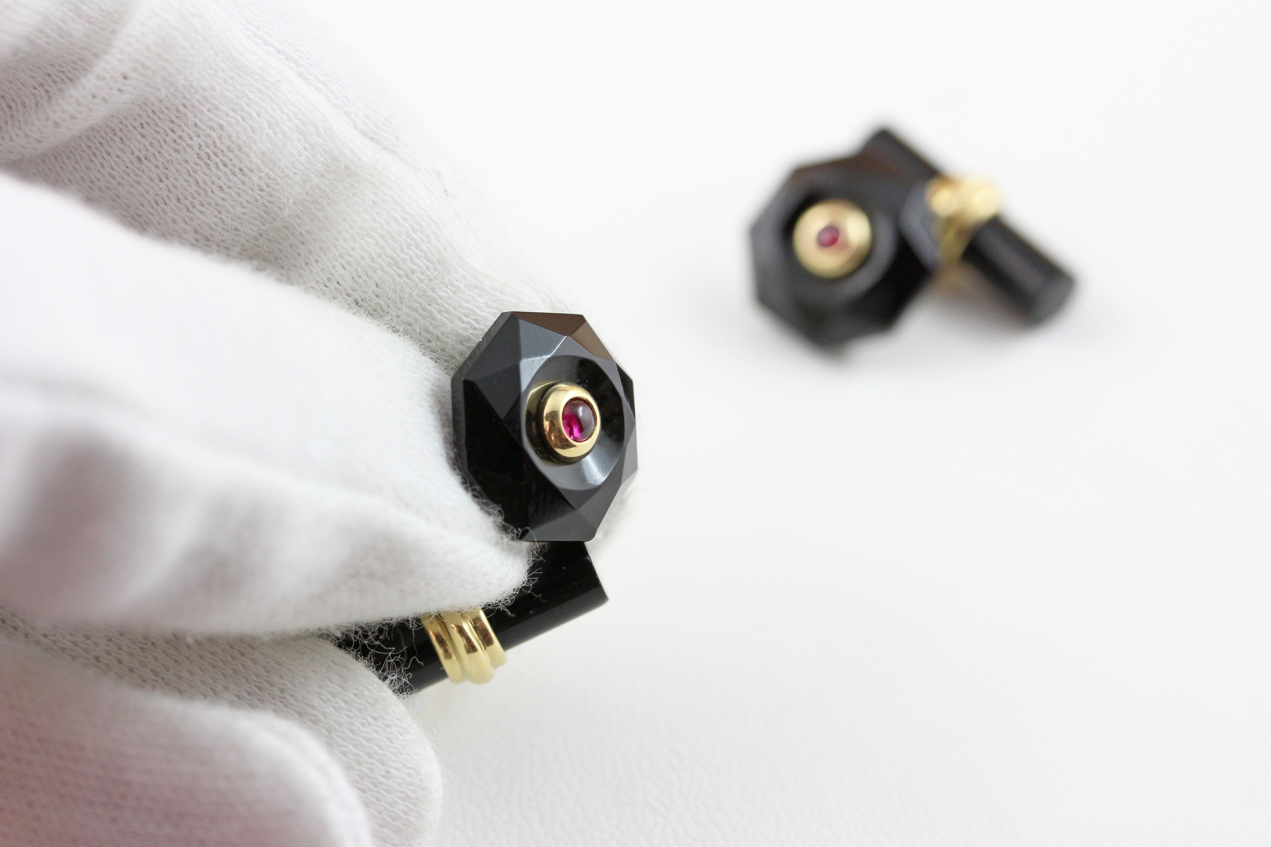 The front face of these exquisite cufflinks has a striking octagonal shape that is convex, multifaceted, and adorned in the center with a cabochon ruby. 
Both the front face and the cylindrical toggle are in onyx, with a post made of 18 karat yellow