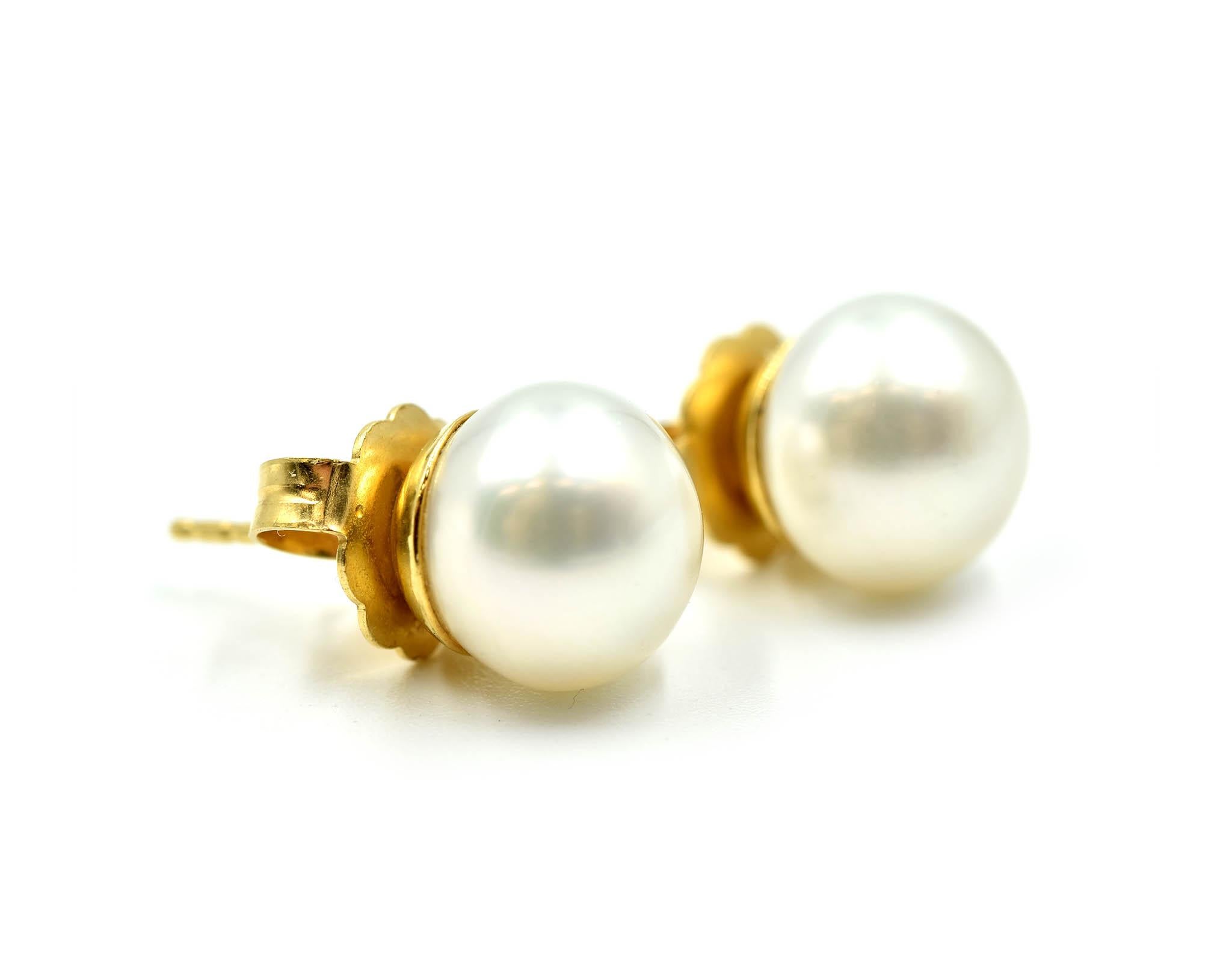 This classic pair is designed in 18k yellow gold. Each stud features a 10.3mm natural pearl. The pearls are white with silver overtones. Each earring is secured with a friction back fastening. The pair weighs 5.7 grams. 