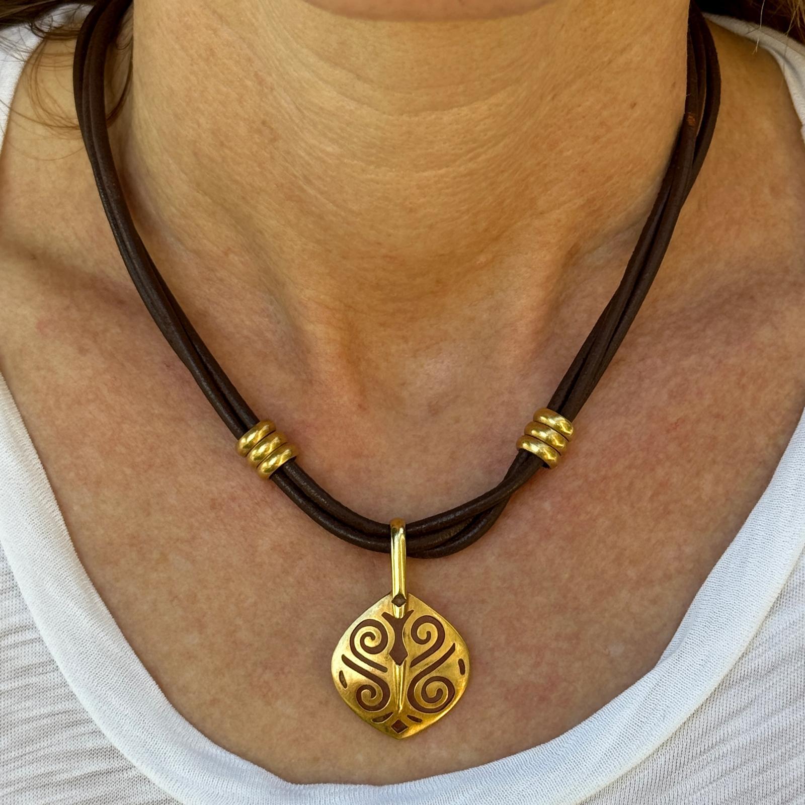 Ce collier remarquable allie l'élégance décontractée à un savoir-faire raffiné. Le pendentif, réalisé en or jaune 18 carats, mesure environ 1 x 1 pouce et est suspendu à un cordon en cuir noir multibrins de 16 pouces. Fini avec un fermoir à crochet