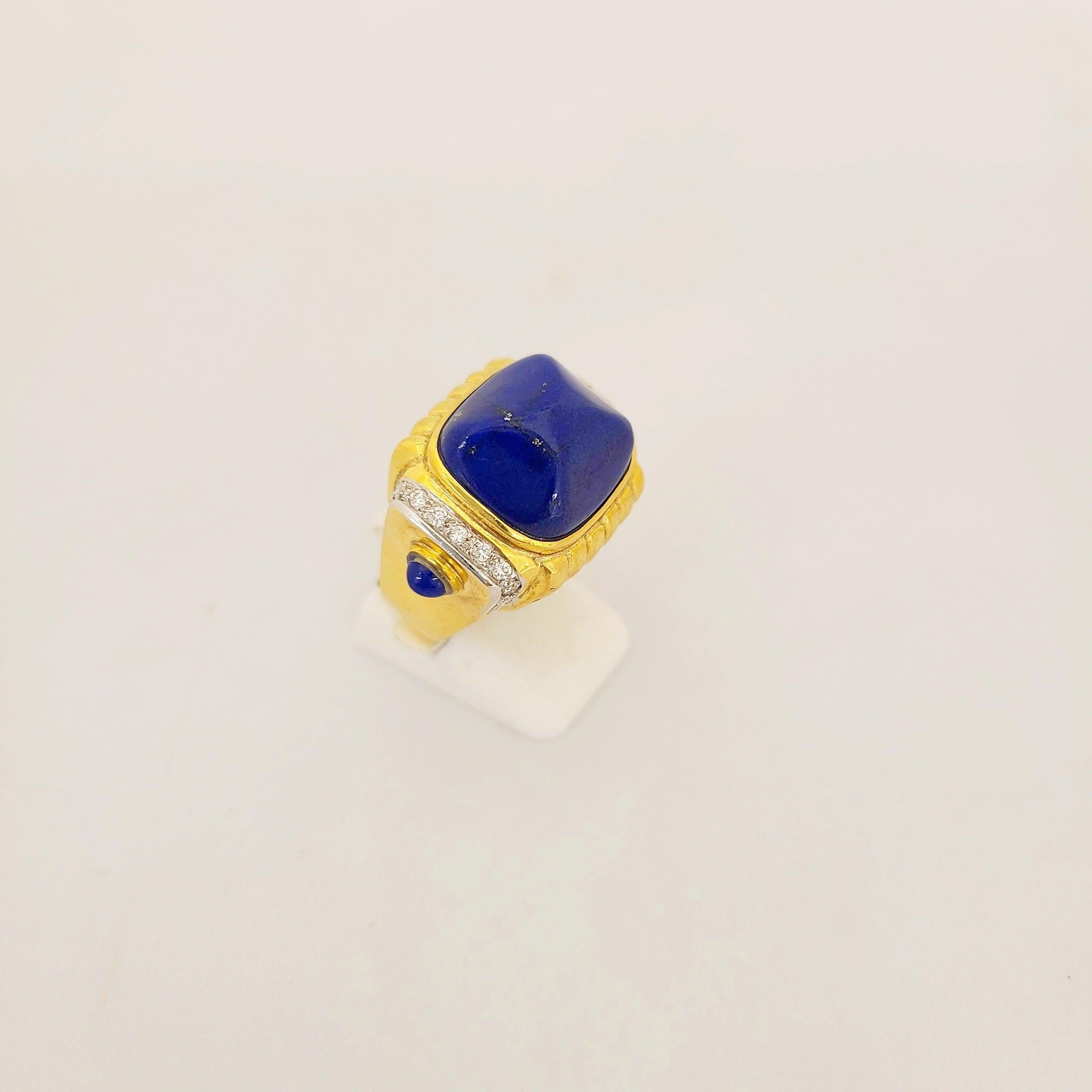 Cette bague en or jaune 18 carats, signée Cellini Jewelers NYC, est conçue avec un grand cabochon Lapis Lazuli en forme de pain de sucre au centre. L'anneau est rehaussé de 0,30 cts. d'or  diamants ronds et 2 cabs de lapis plus petits.
Estampillé