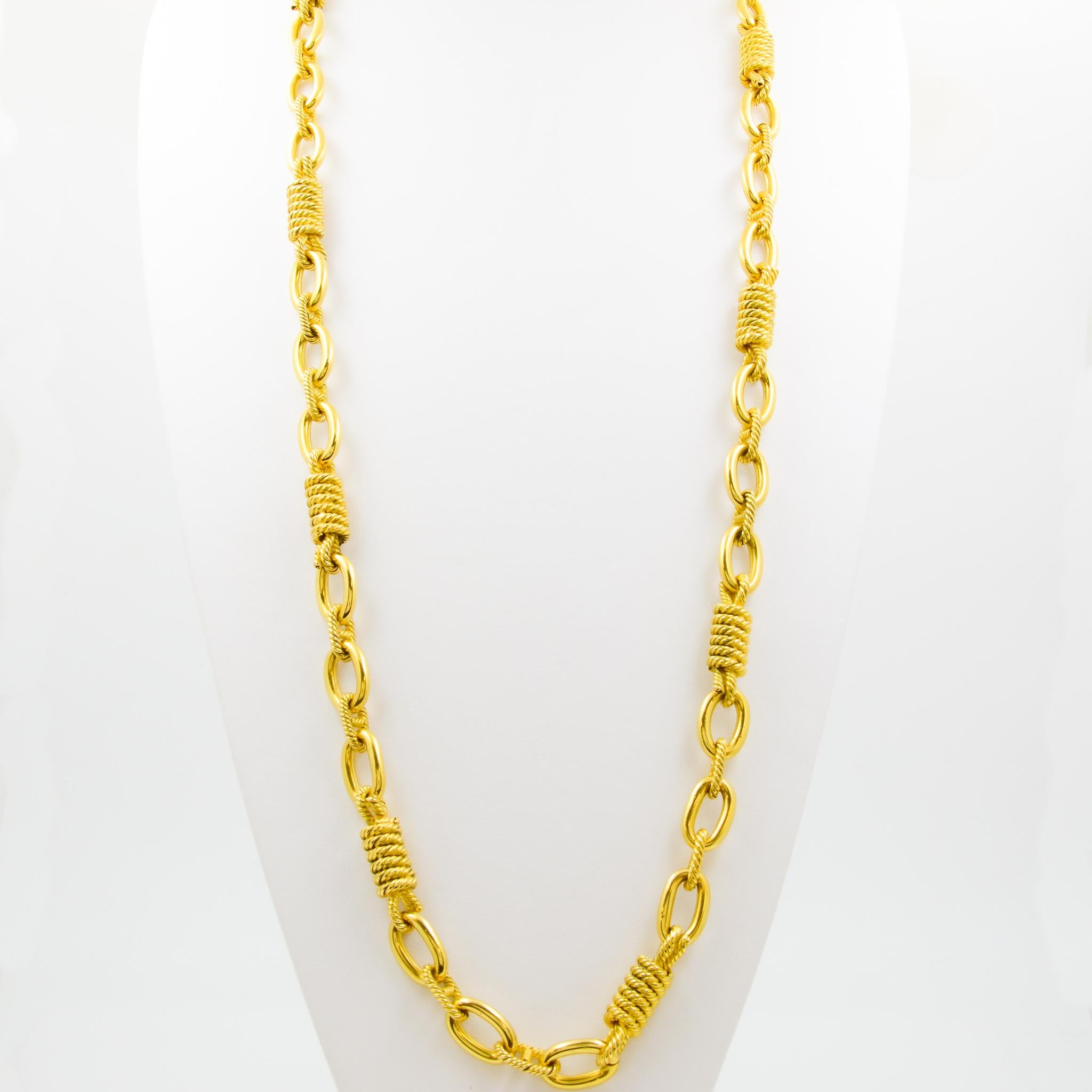 This 18 karat yellow gold chain necklace features textured wrapped rope links alternating with polished finish oval links. The necklace measures 36 inches long and does not have a clasp, perfect for draping and layering.
