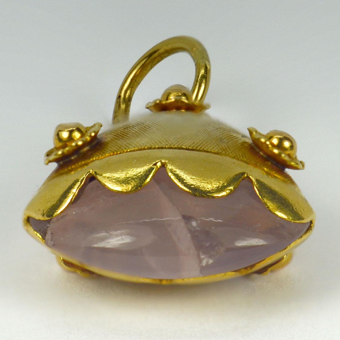 An 18 karat (18K) yellow gold charm pendant designed as a flaring oval cylinder with cross-hatch and rosette decoration, mounted to the base with an oval rose quartz cabochon (fractured). Stamped with the owl mark for French import and 18 karat