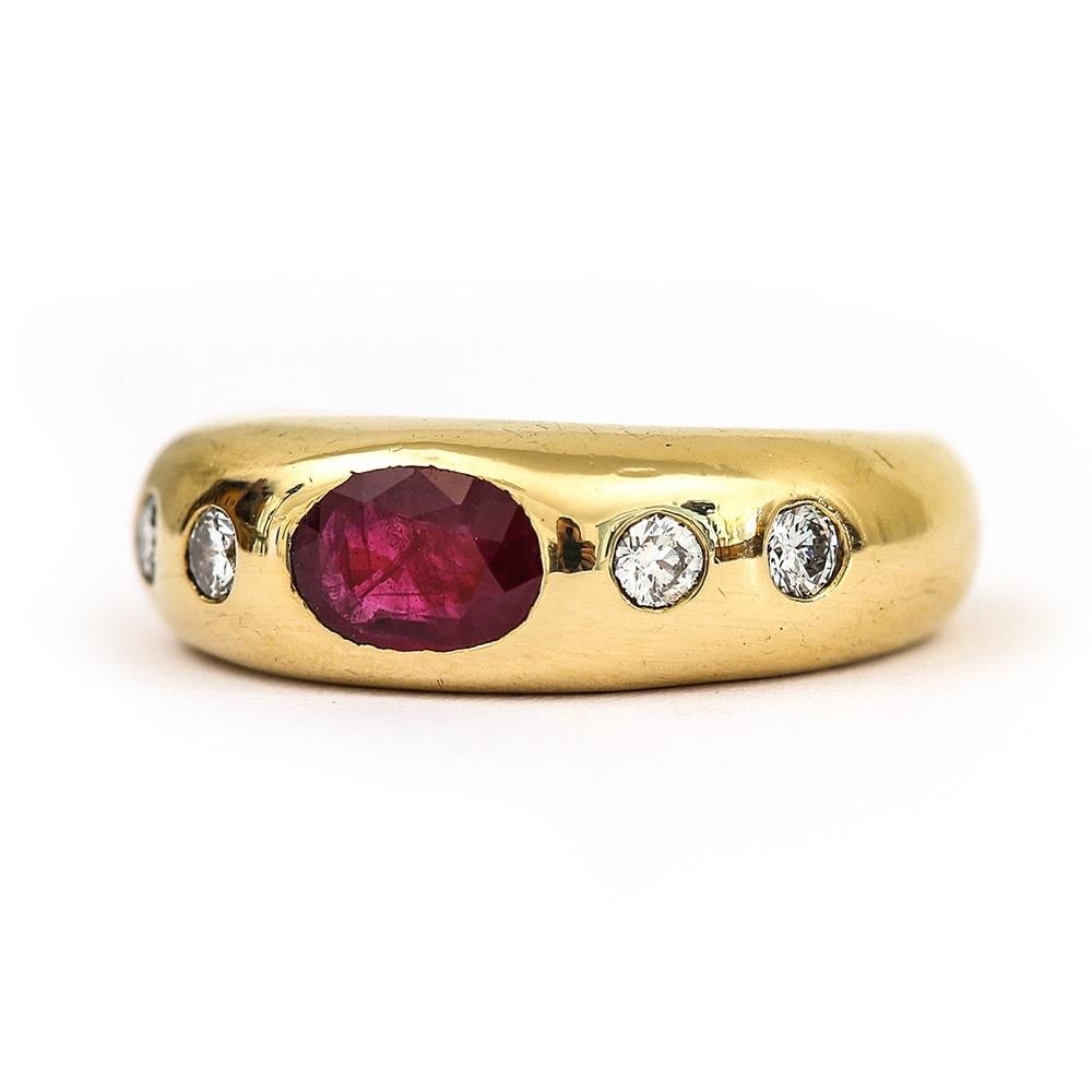 An 18 karat yellow gold gold Roman set faceted oval ruby gypsy style ring, with four flush set brilliant cut 0.05ct brilliant cut diamonds. The ring is reminiscent of the Cartier style. A solid 7.92 grams in weight this ring is an attractive