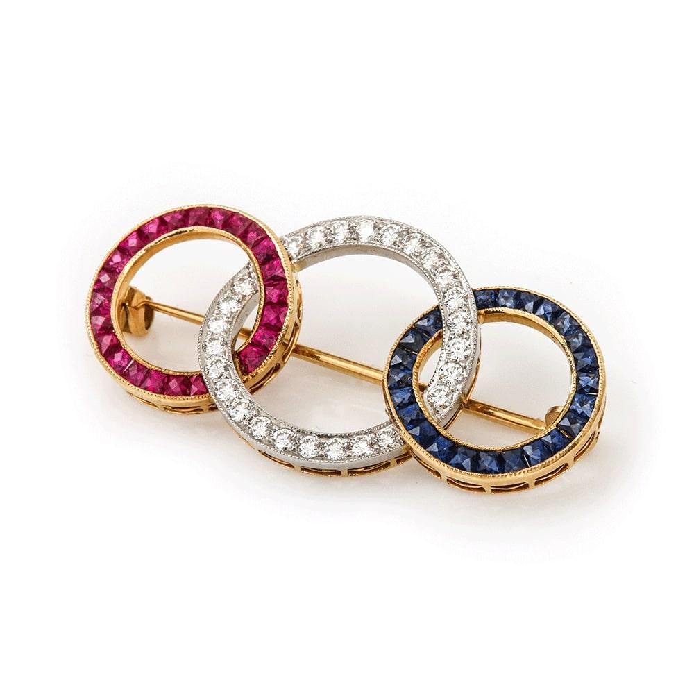 A striking ruby, diamond & sapphire 18k brooch designed as three interwoven rings made in the 1950s.

Comprising 25 0.01ct matched brilliant cut diamonds, totalling est. 0.25ct. Also 23 calibre-cut, matched rubies & sapphires form the other circles.