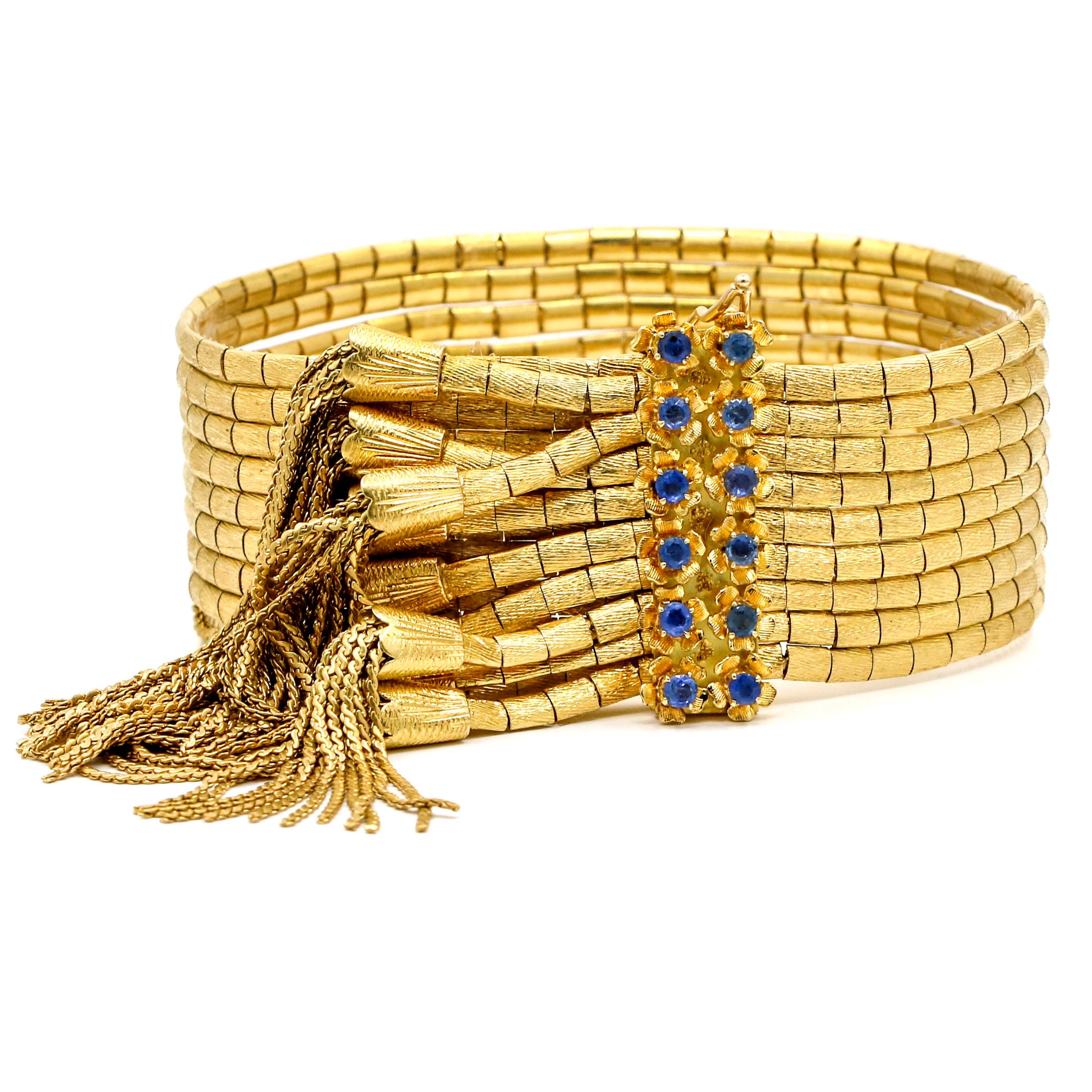 Multi-strand bracelet in 18-karat yellow gold with blue sapphires. The bracelet has 9 strands that are made out of textured gold links with tassel ends. The clasp has 12 round cut natural sapphires. Made in Italy. Signed 86VI. 

Size, Large (fits a