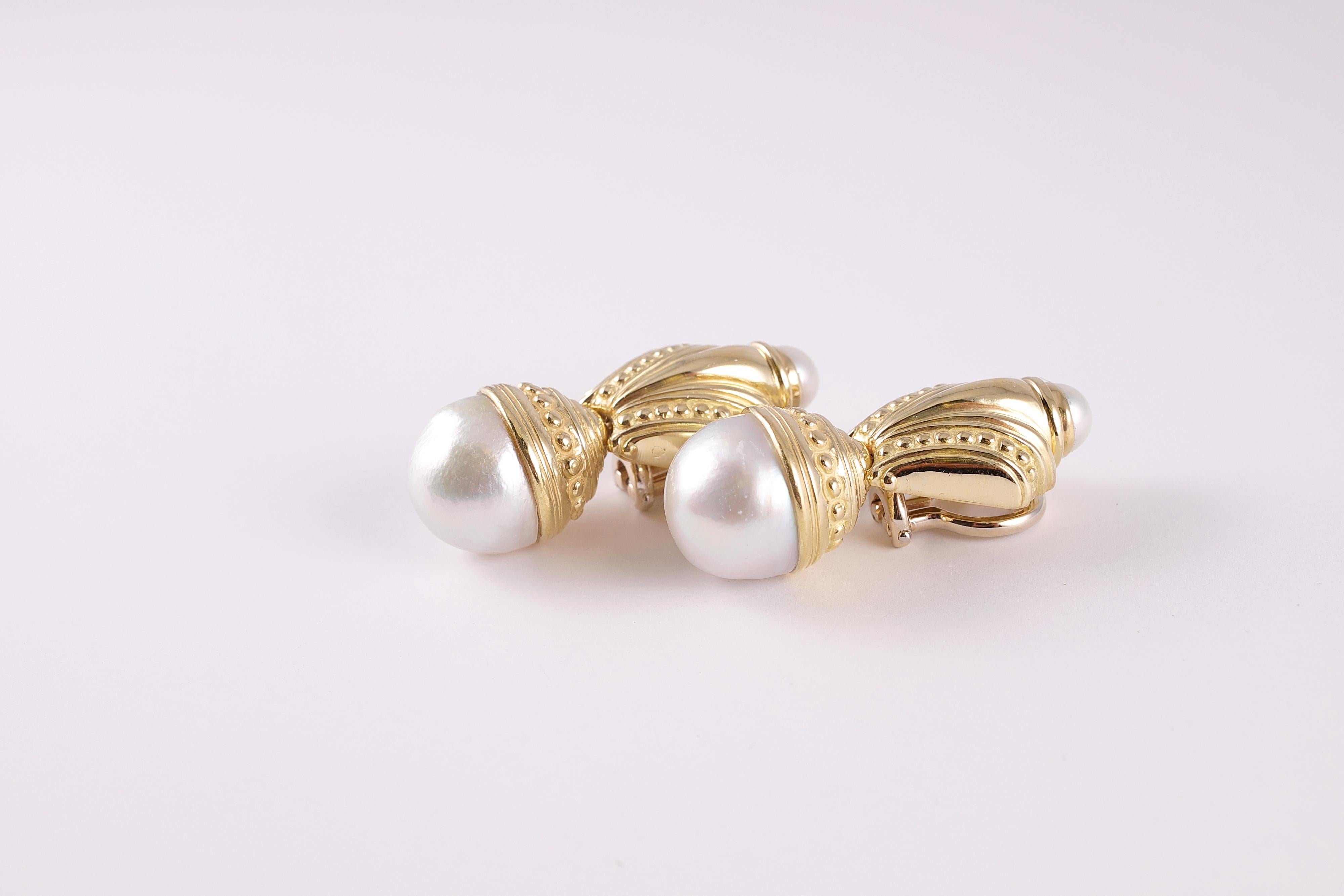 By jewelry designer Matthew Trent, these classic earrings are composed of 18 karat yellow gold and each supports one 3/4 round South Sea cultured pearl and one bezel-set, round pearl.  The South Sea pearls measure 14.90 mm each and the cultured