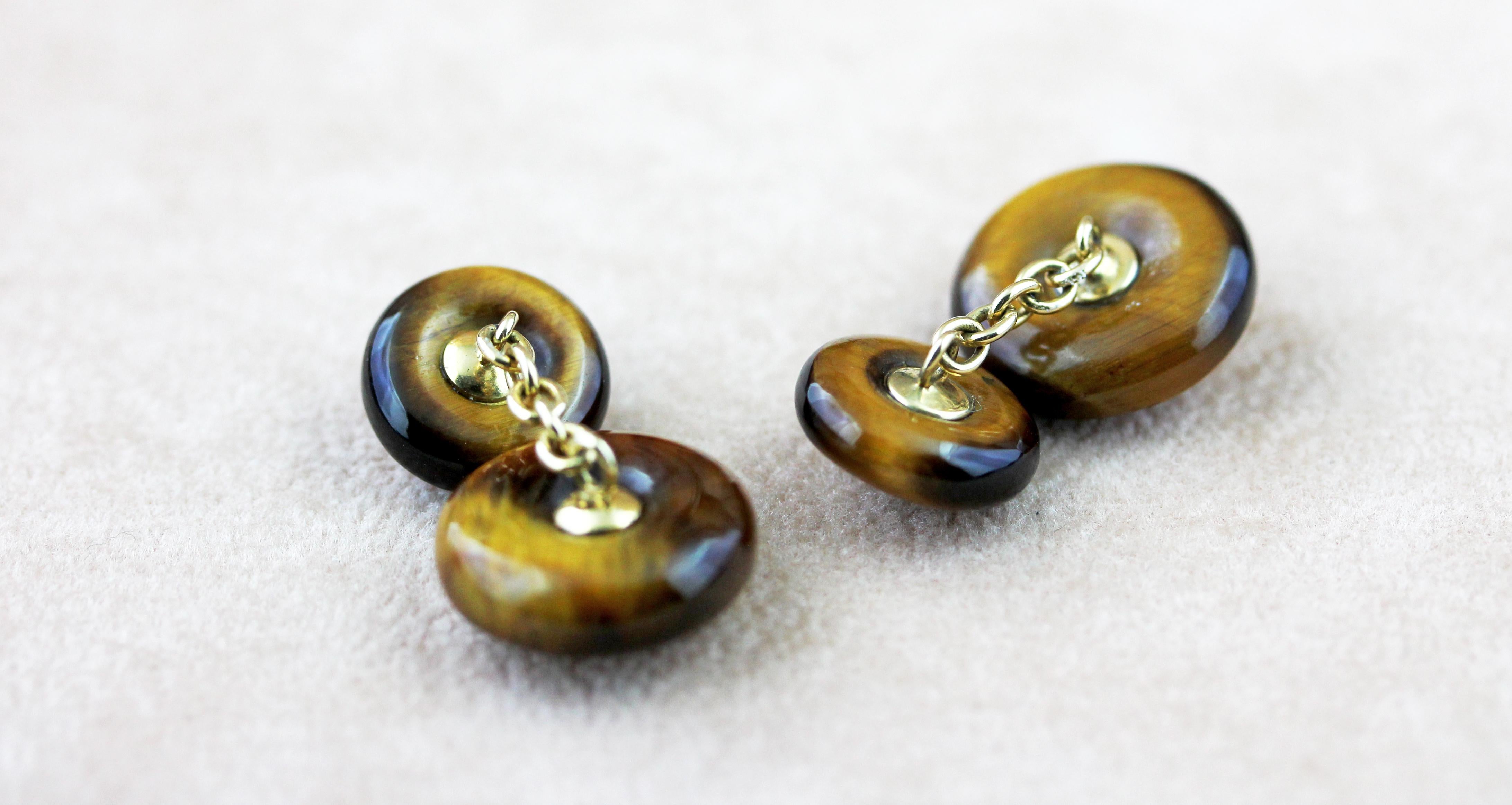 This striking pair of cufflinks is made entirely in tiger’s eye stone and comprises identically shaped front face and toggle, carved as circles whose warm, dark color is accented with a cabochon ruby in the center, mounted in 18k yellow gold.